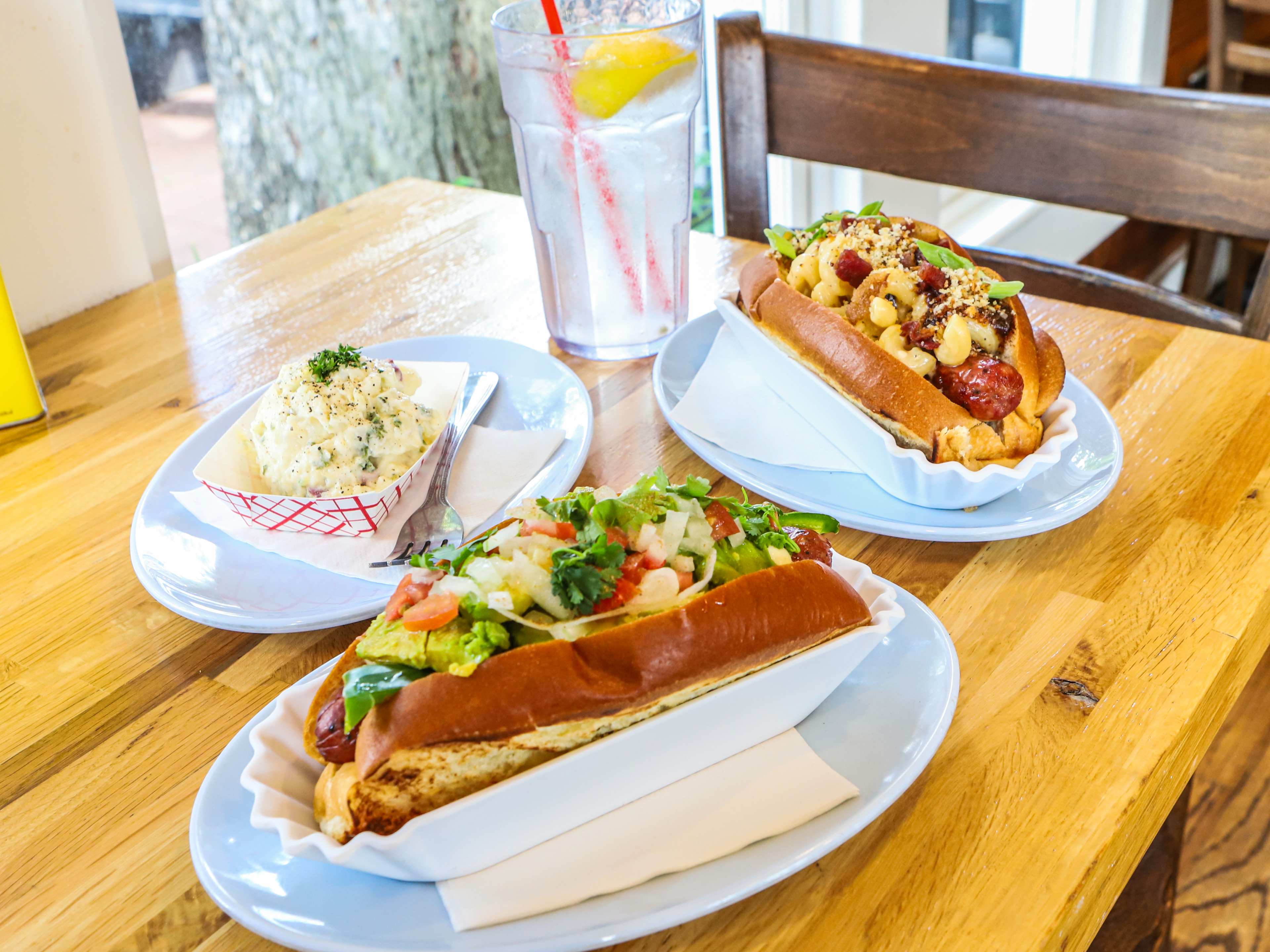 A spread of two hot dogs, potato salad, and a drink on a table at Good Dog Houston.