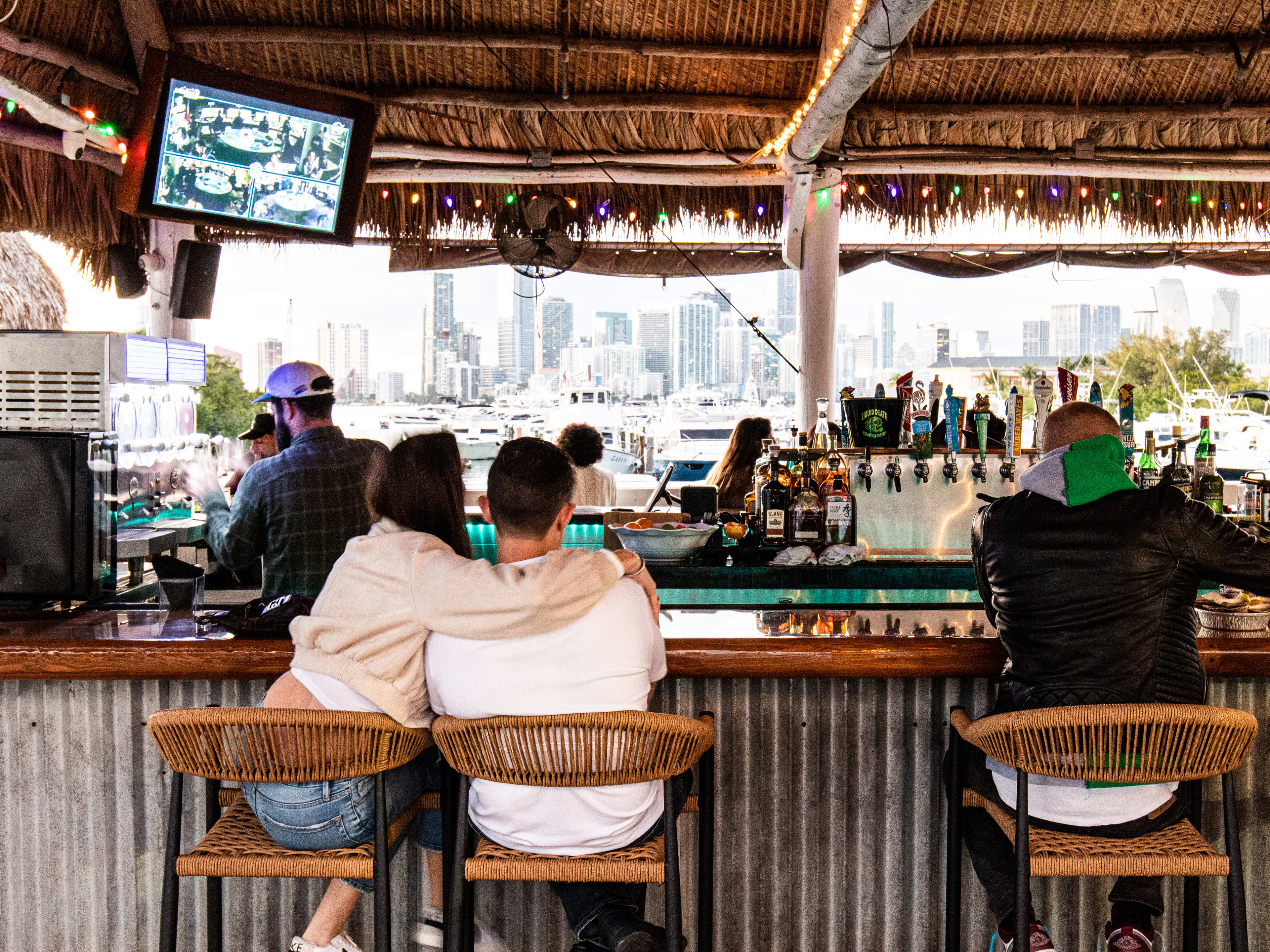 People sit at an outdoor bar facing the water.