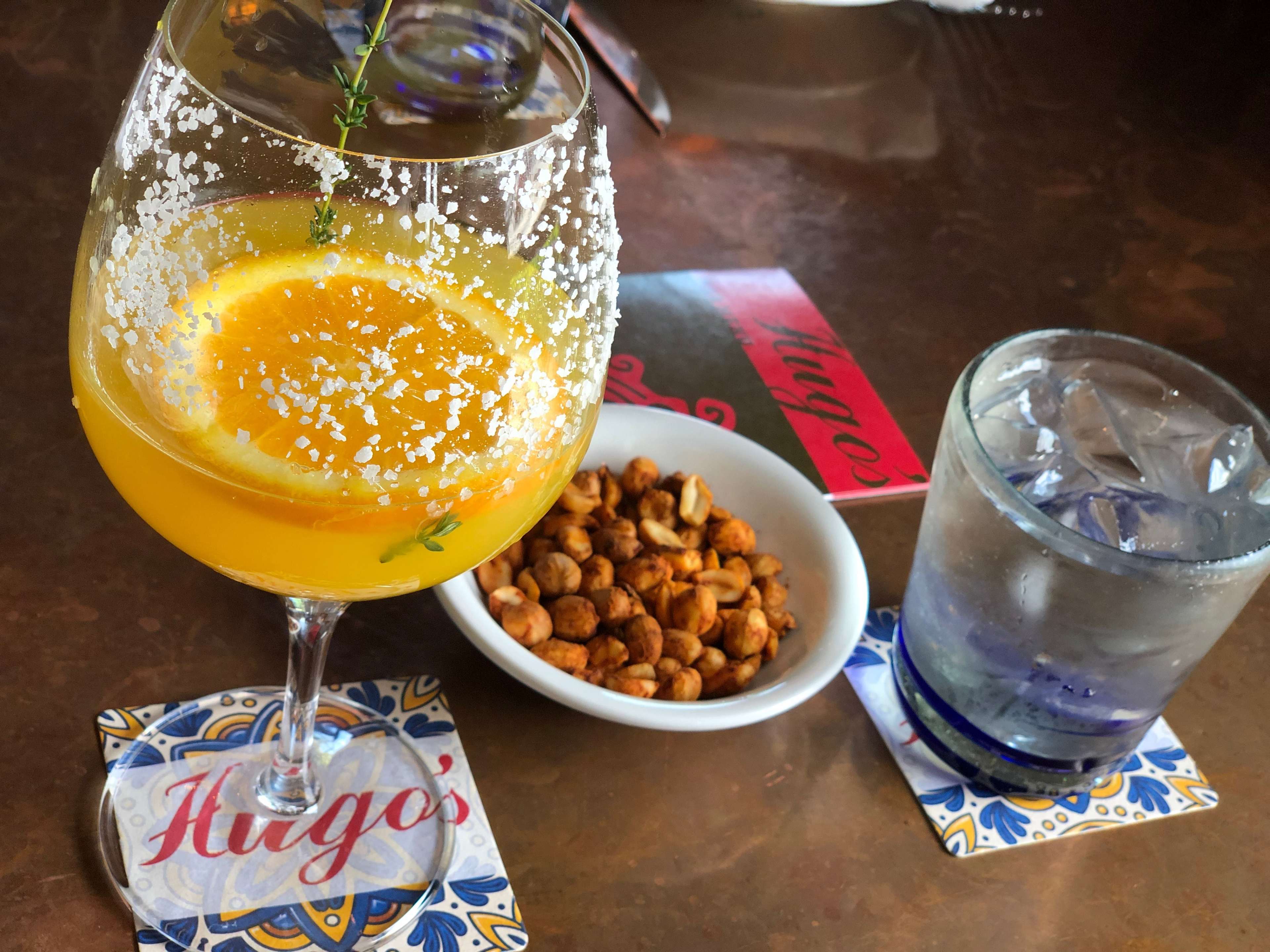 honey colored margarita in a wine glass with a salt rim next to bar snacks