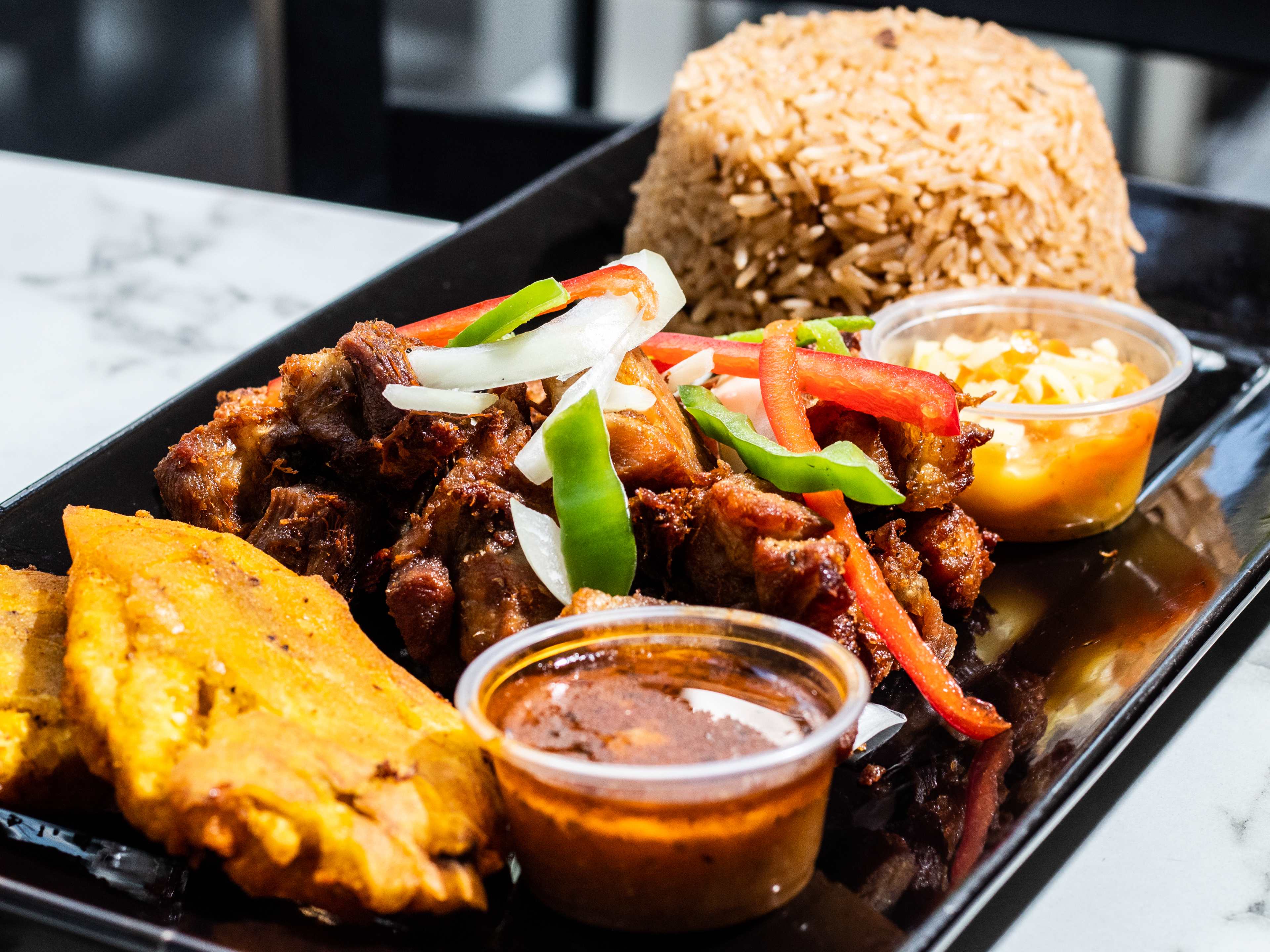 Griot and a pile of rice on a rectangular black plate.