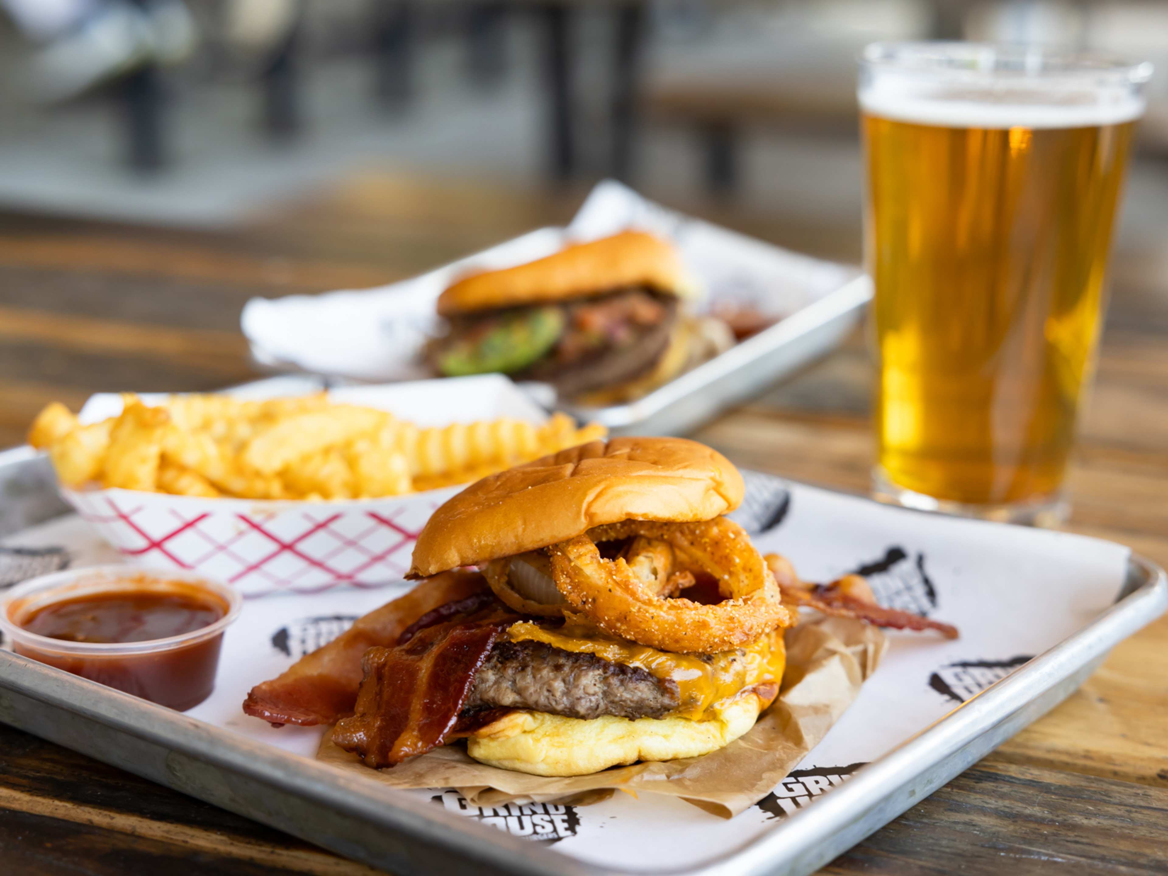 burger with onion rings on tray next to beer and paper tray of crinkle fries