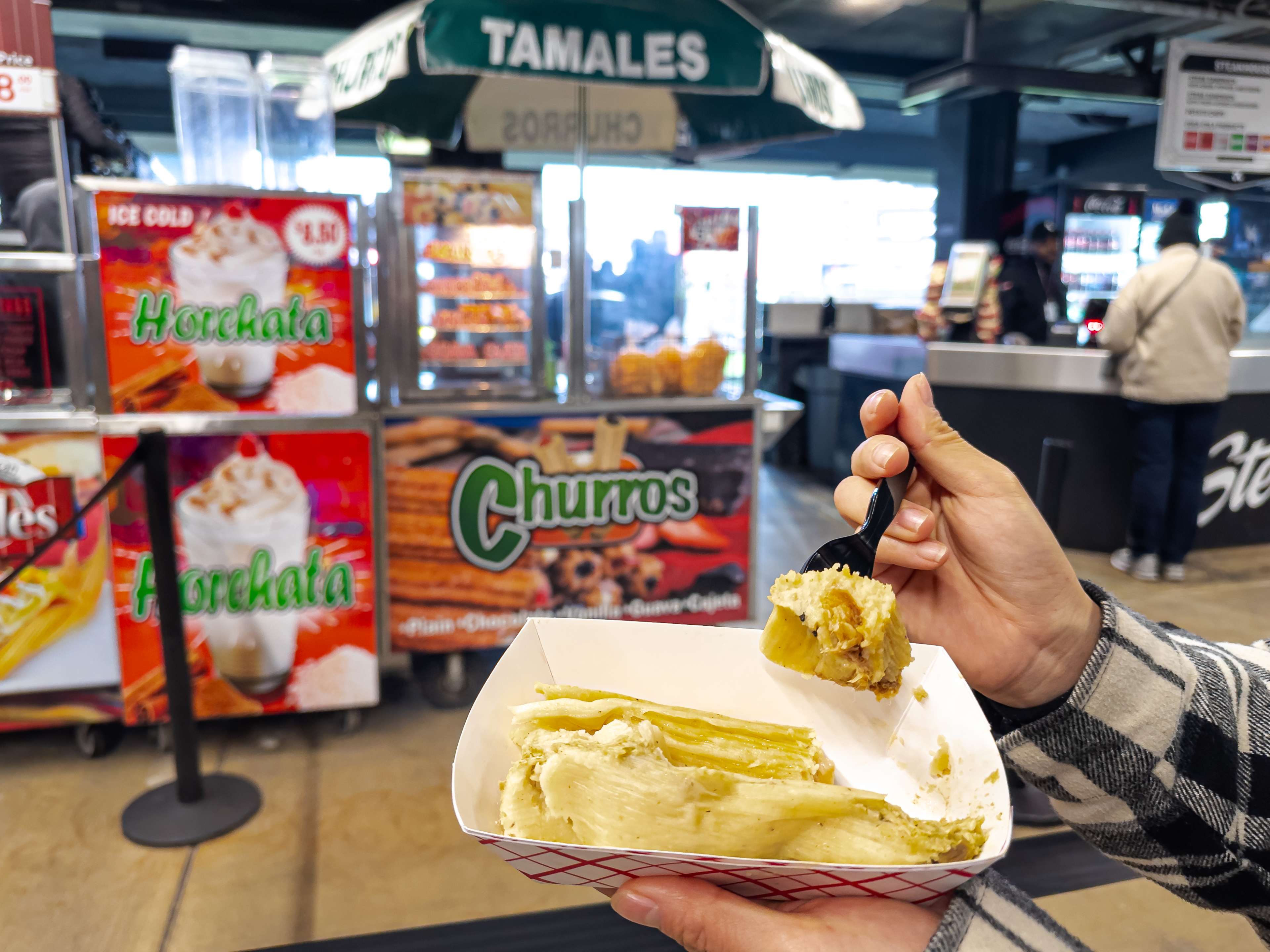 Tamales held up in front of an elotes-churros-tamales cart at Guaranteed Rate Field