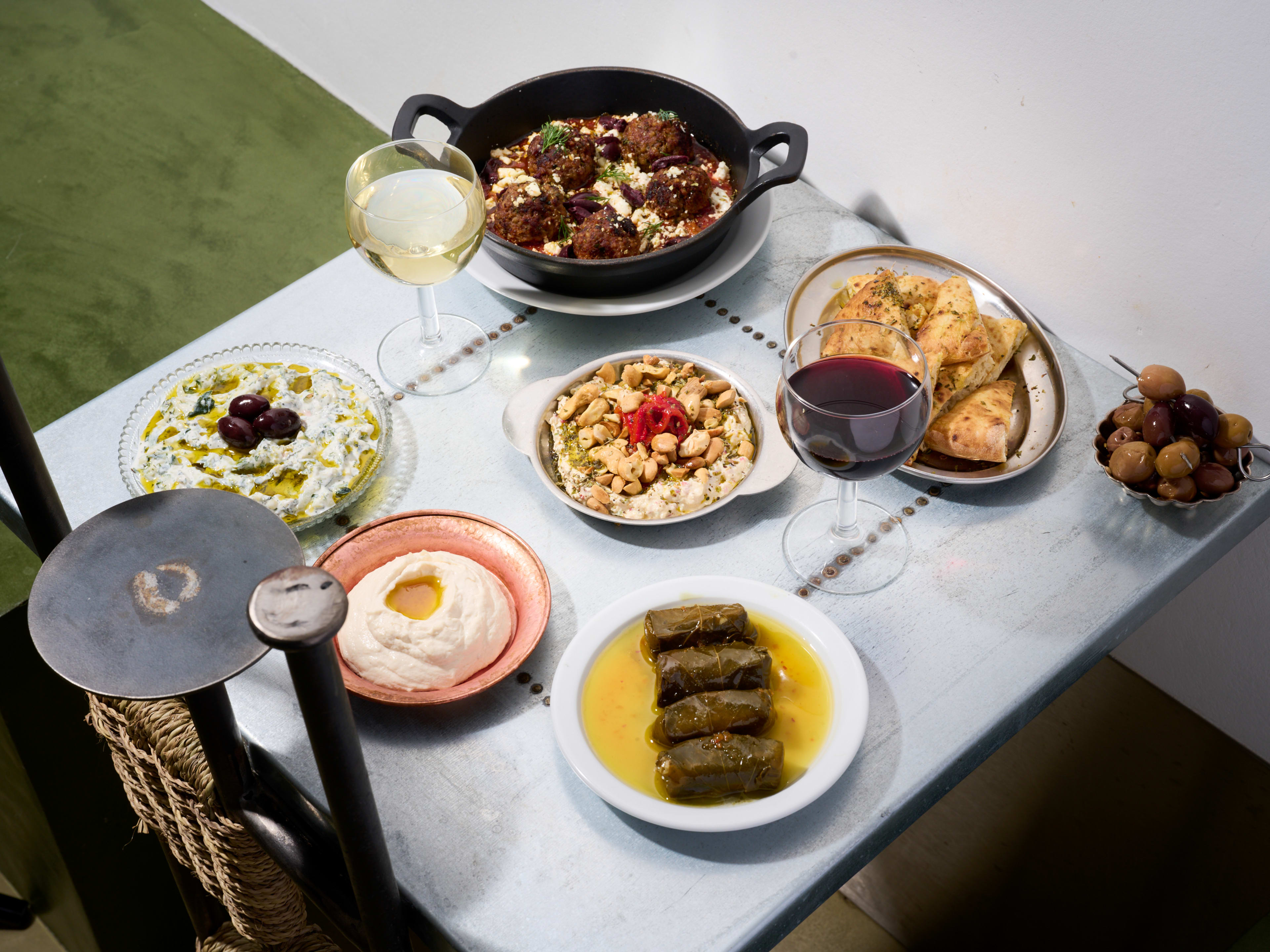 Spread of small Greek dishes with glasses of white and red wine on table at Taverna Paris