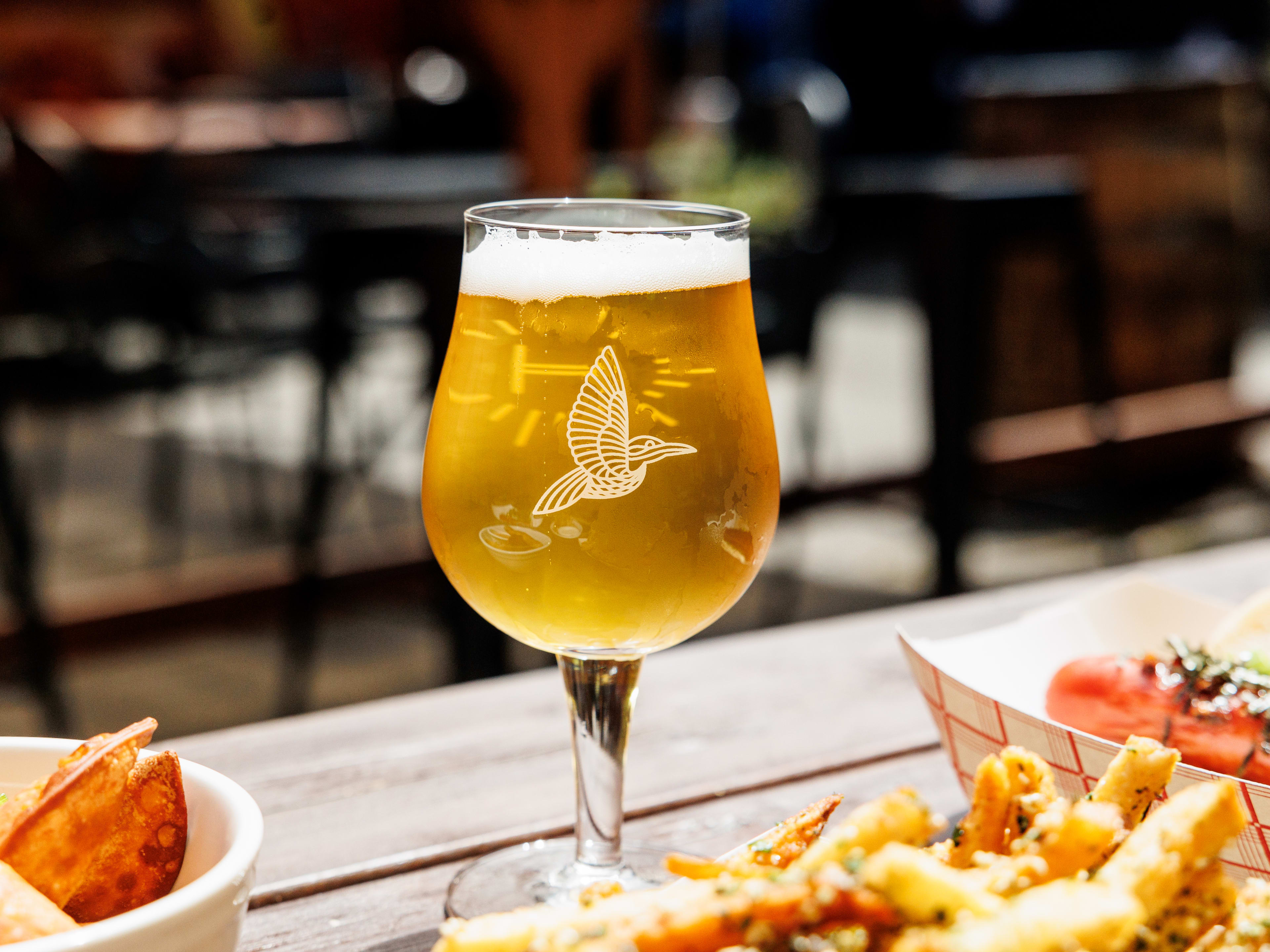 beer in stemmed glass surrounded by paper trays of food