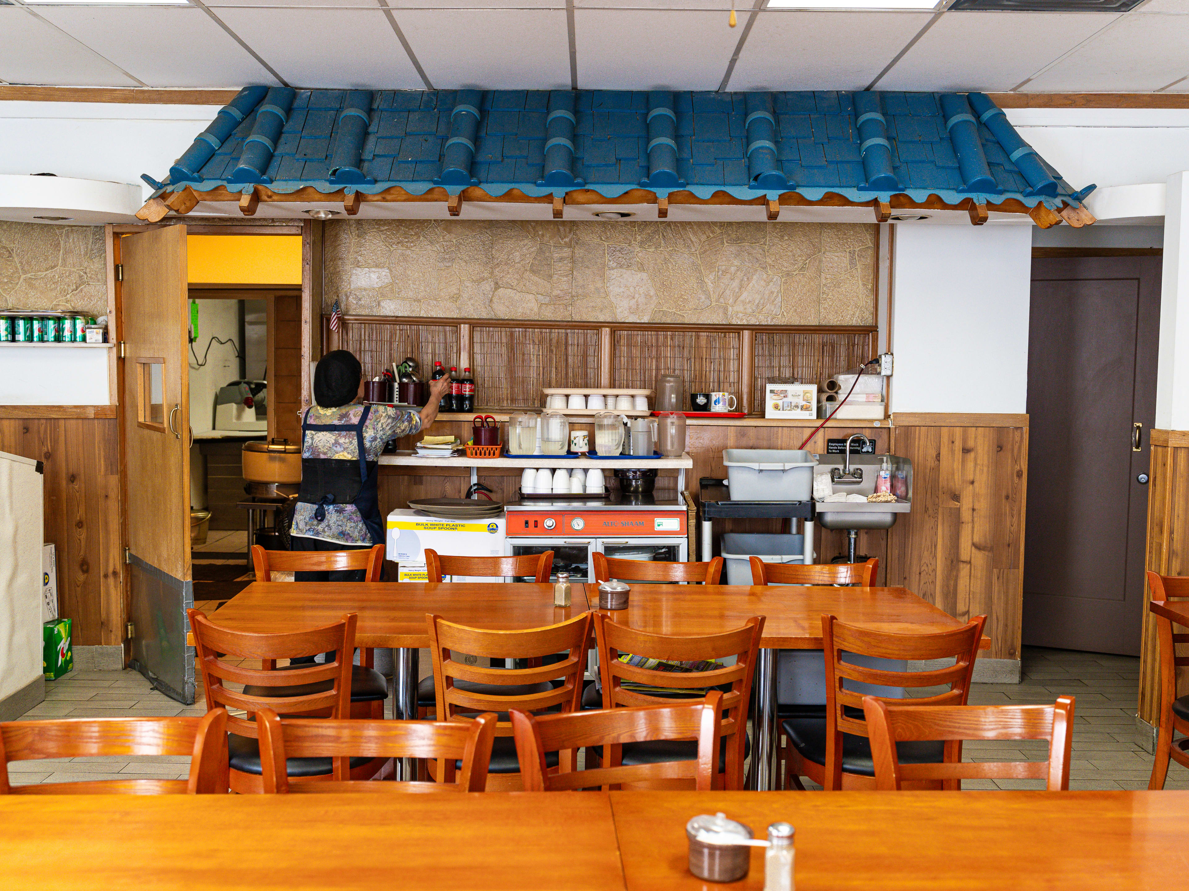 A small dining room with wooden tables and a decorative Korean-style roofing attached to the wall.