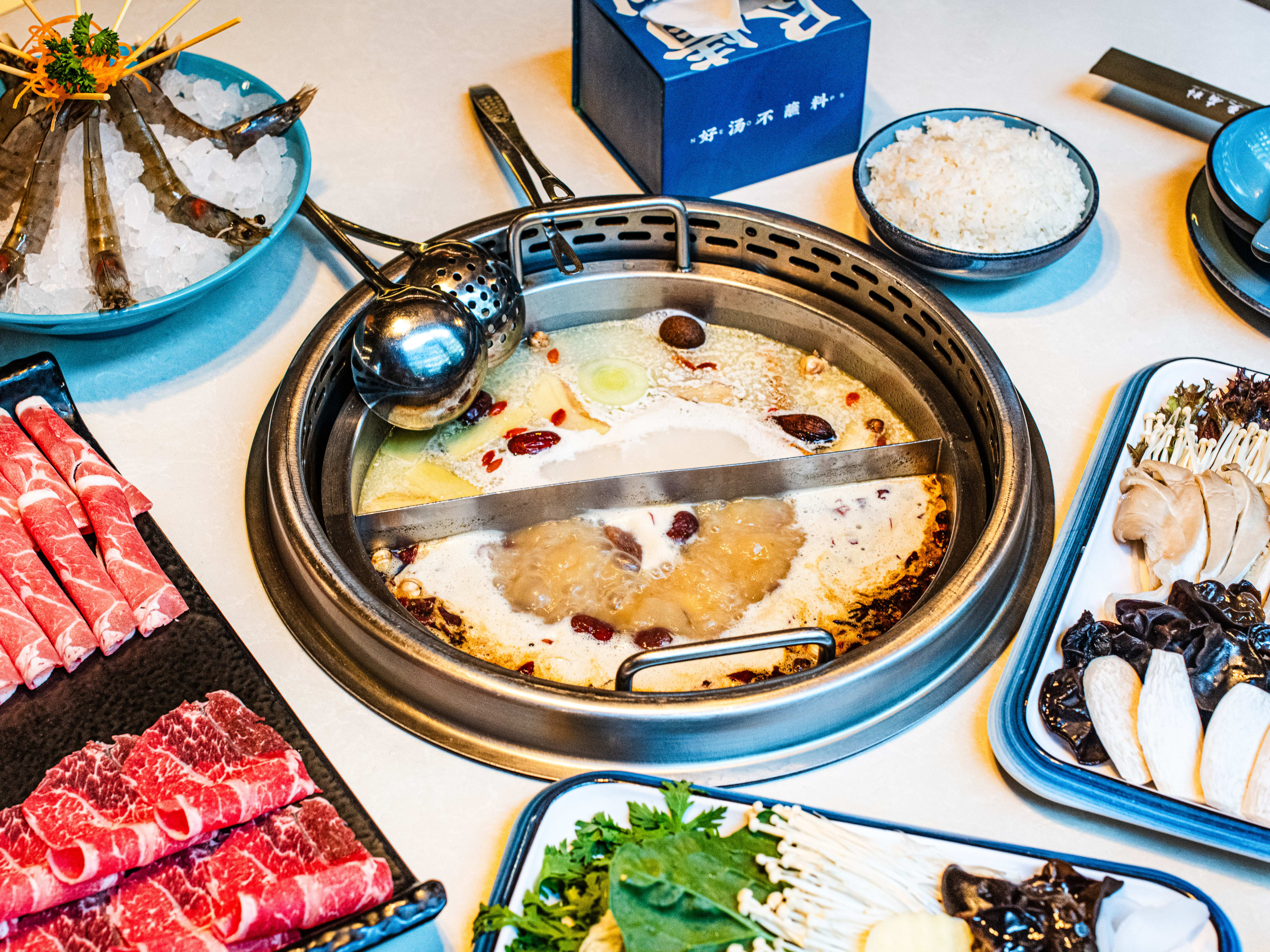 A spread of raw vegetables, fish, and meat with boiling broths in the middle at Happy Lamb Hotpot.