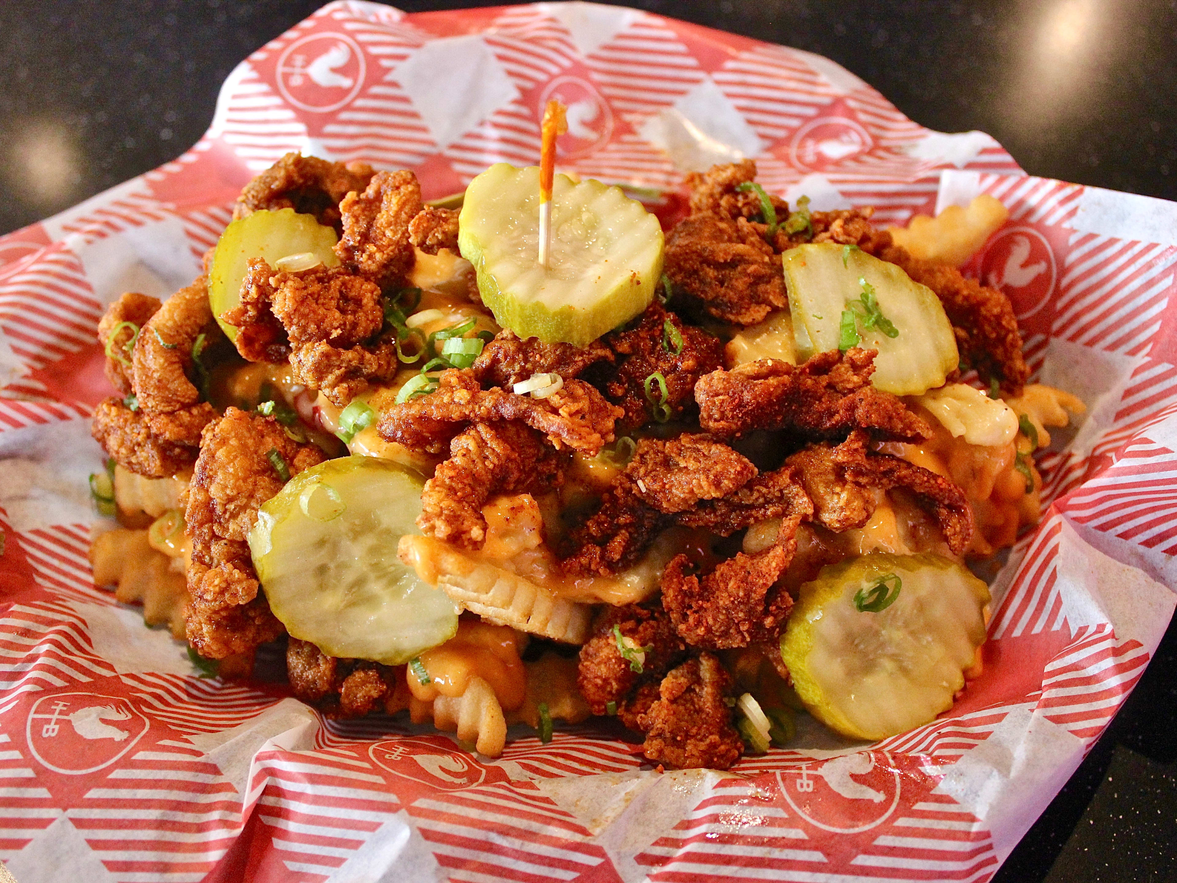 A pile of crinkle french fries topped with chicken and pickles.