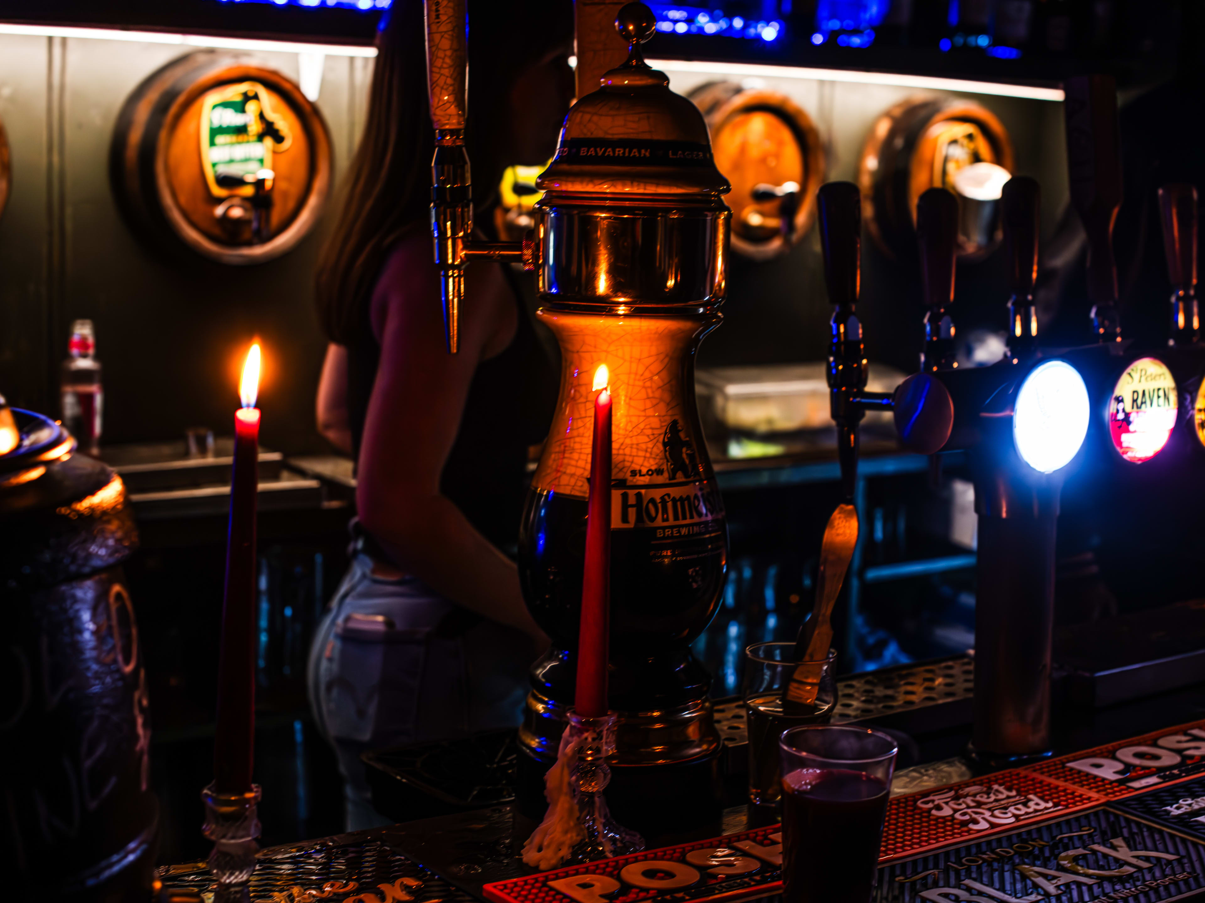 The bar at The Holy Tavern lit by candles and showing barrels of ale in the background.