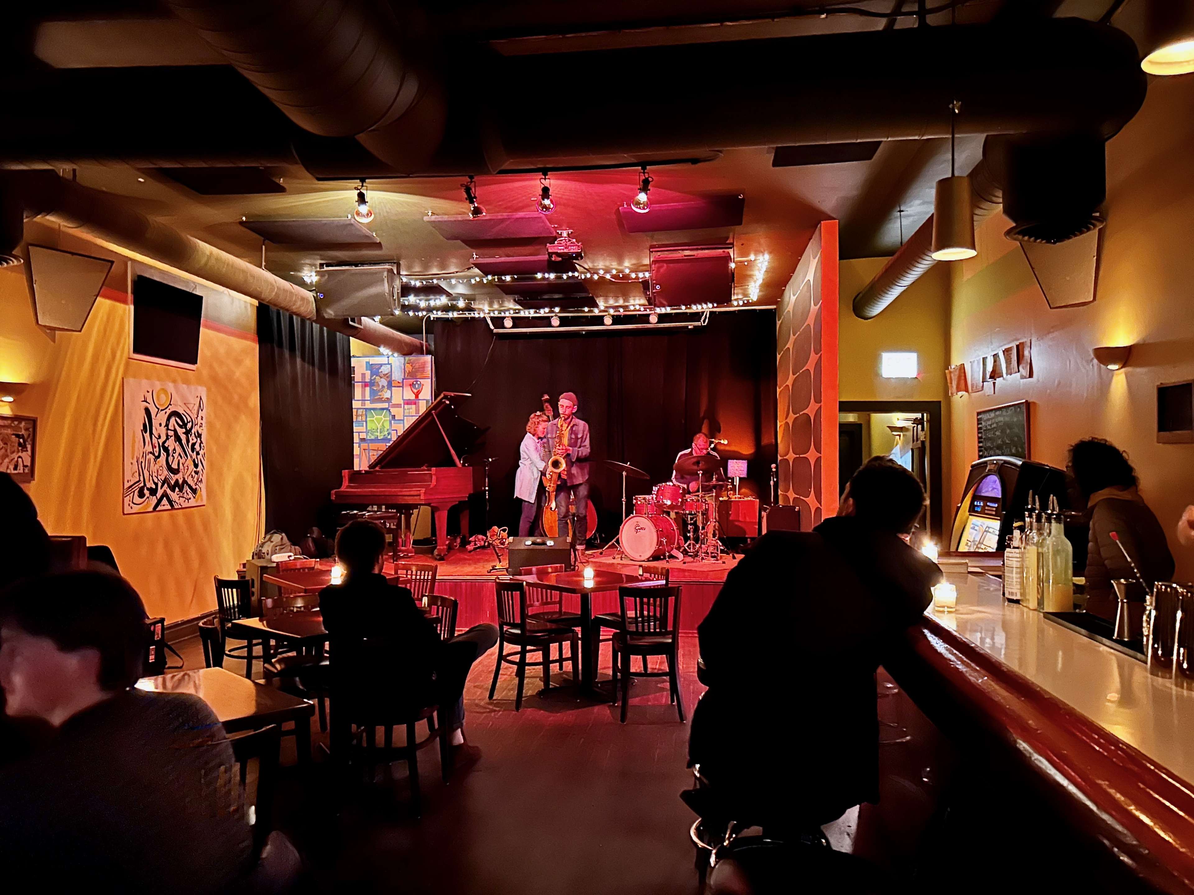 A dimly lit bar with a jazz trio performing on a stage at the back.