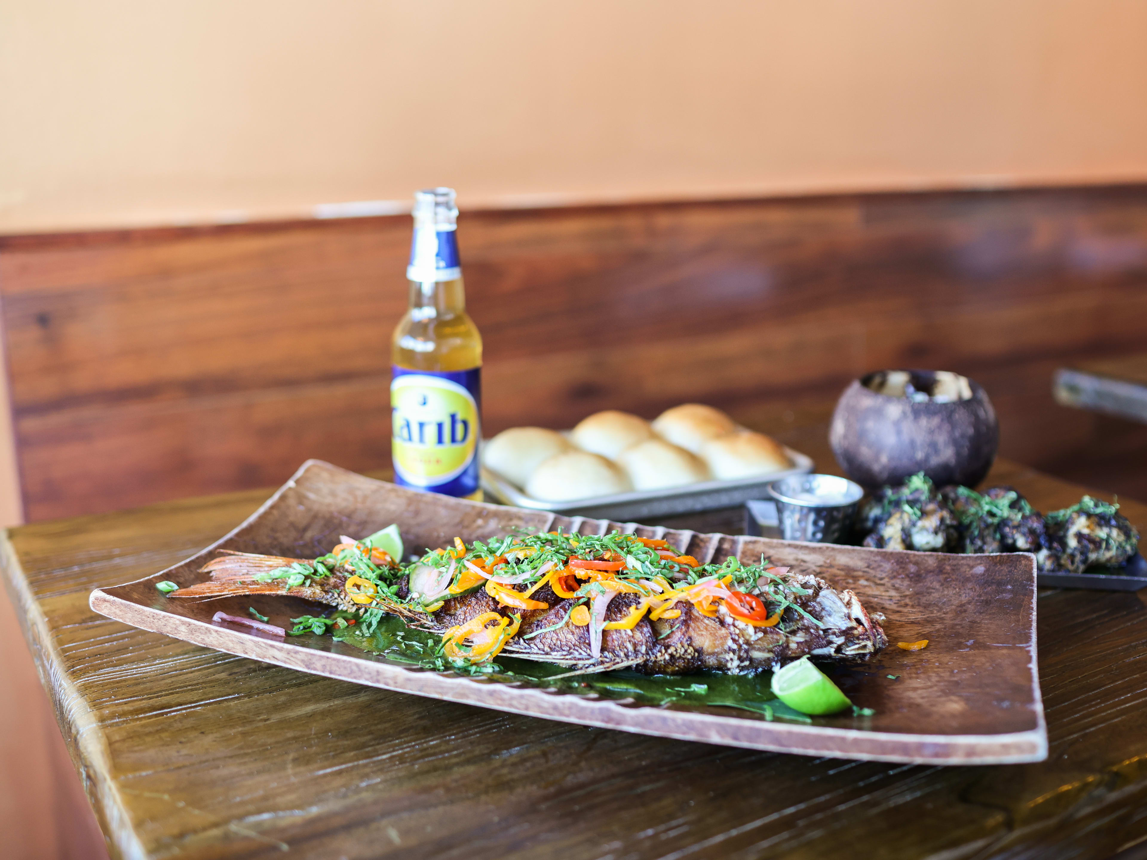 Wooden platter with whole fried fish, carribbean soda, and other tropical small plates