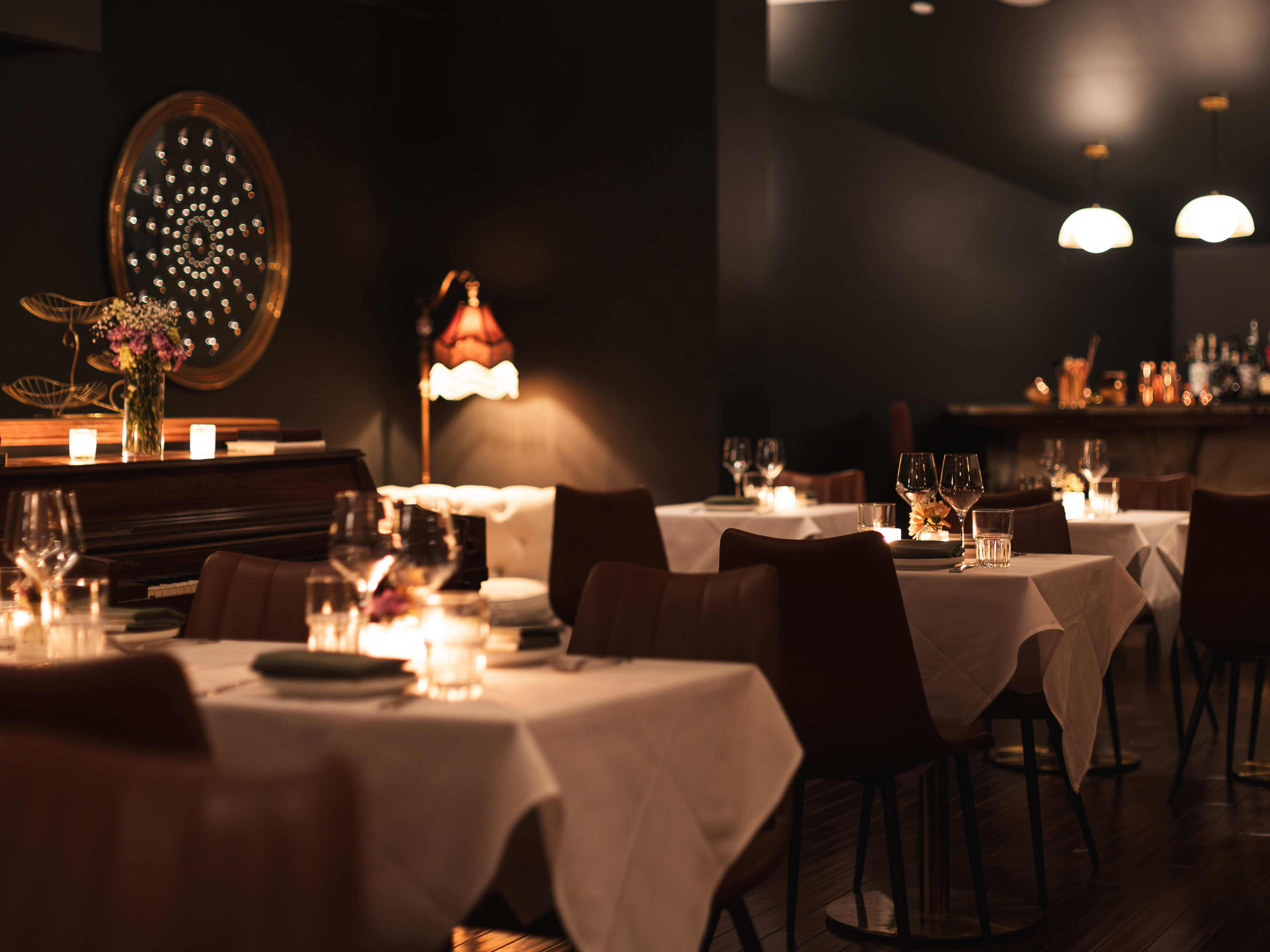 A dark restaurant with white tablecloths and a piano in the corner.