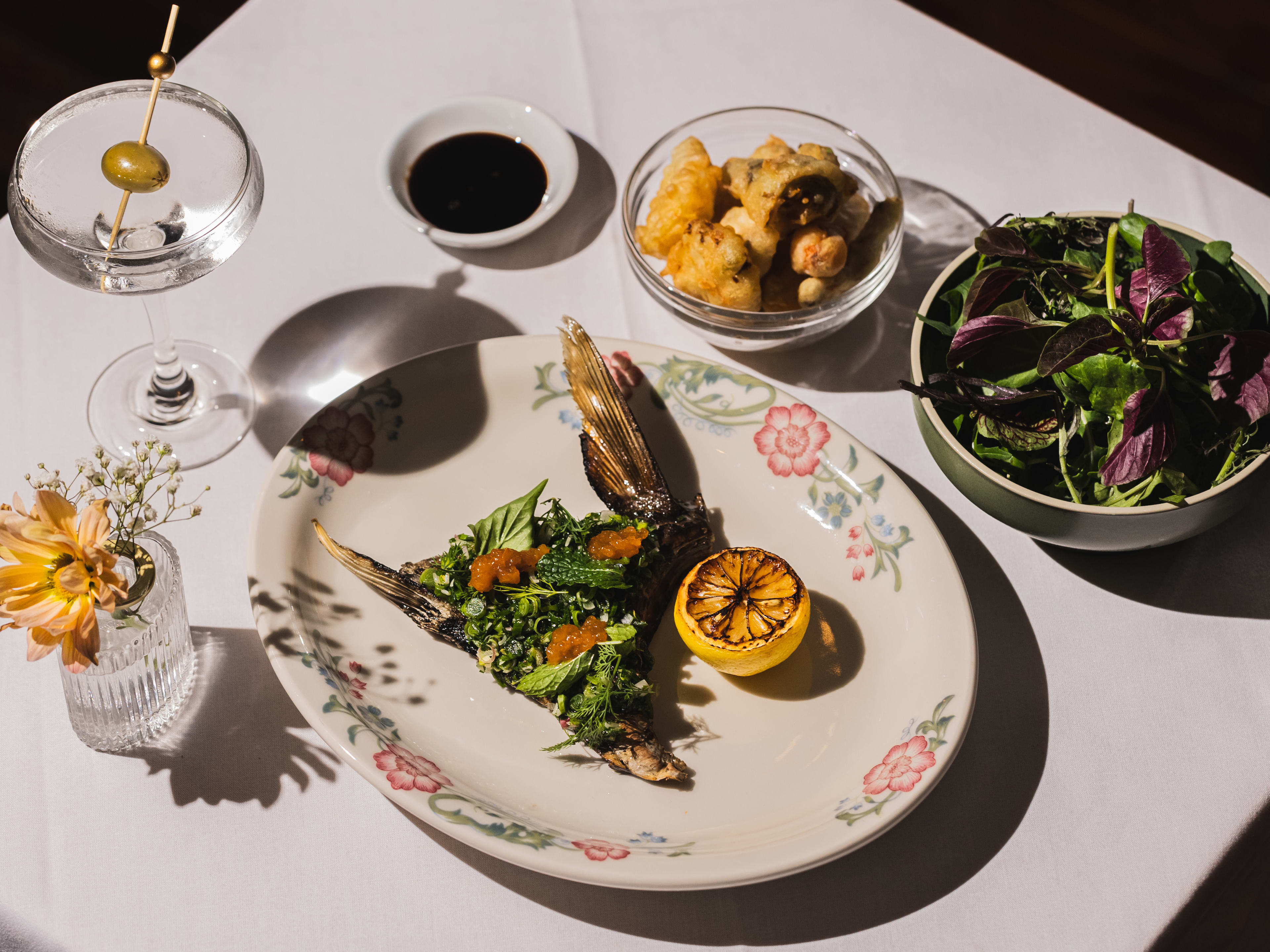 A piece of fish on a plate, with a martini and salad on the side.