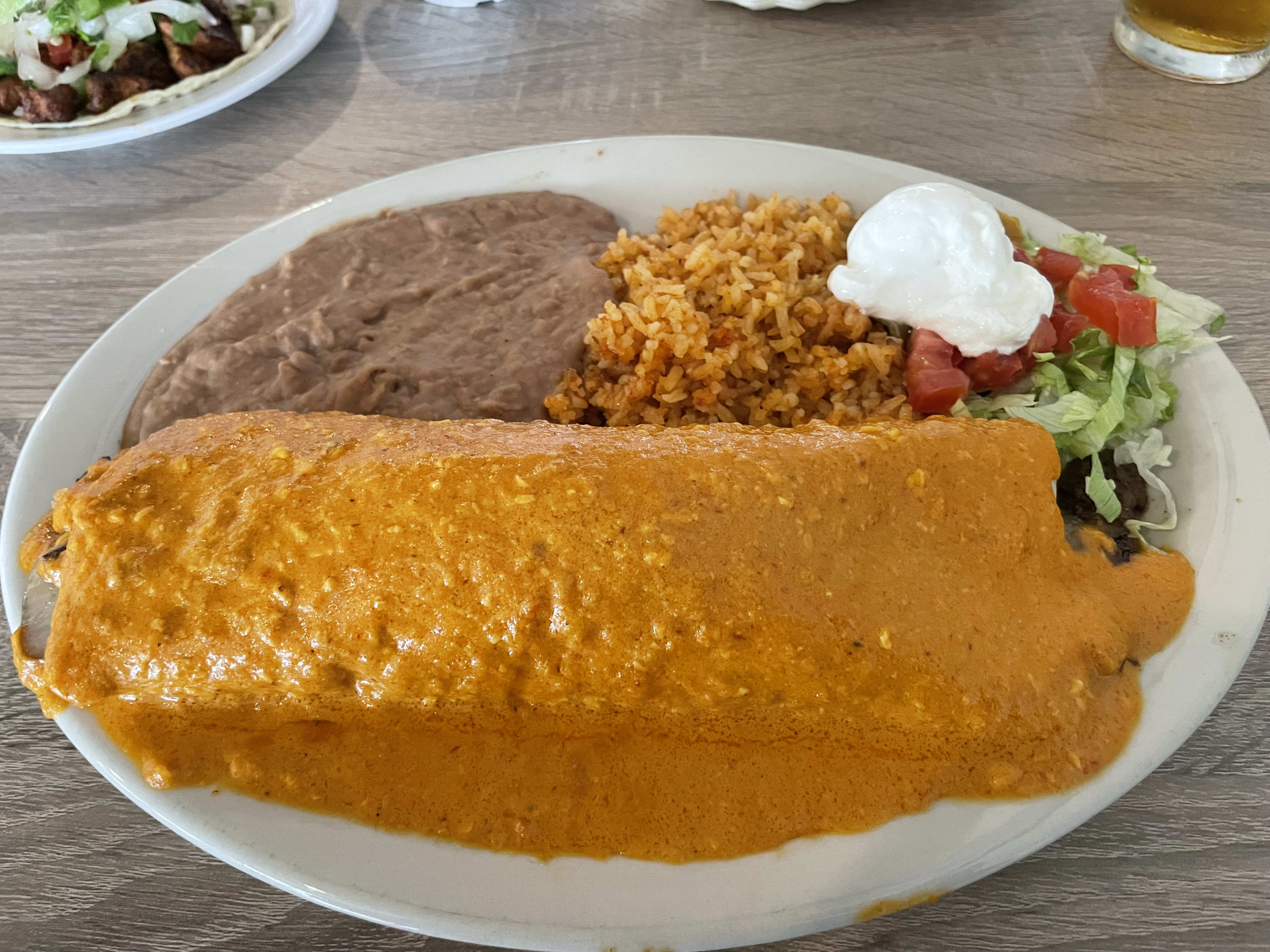 Burrito drenched in sauce with side of beans and rice.