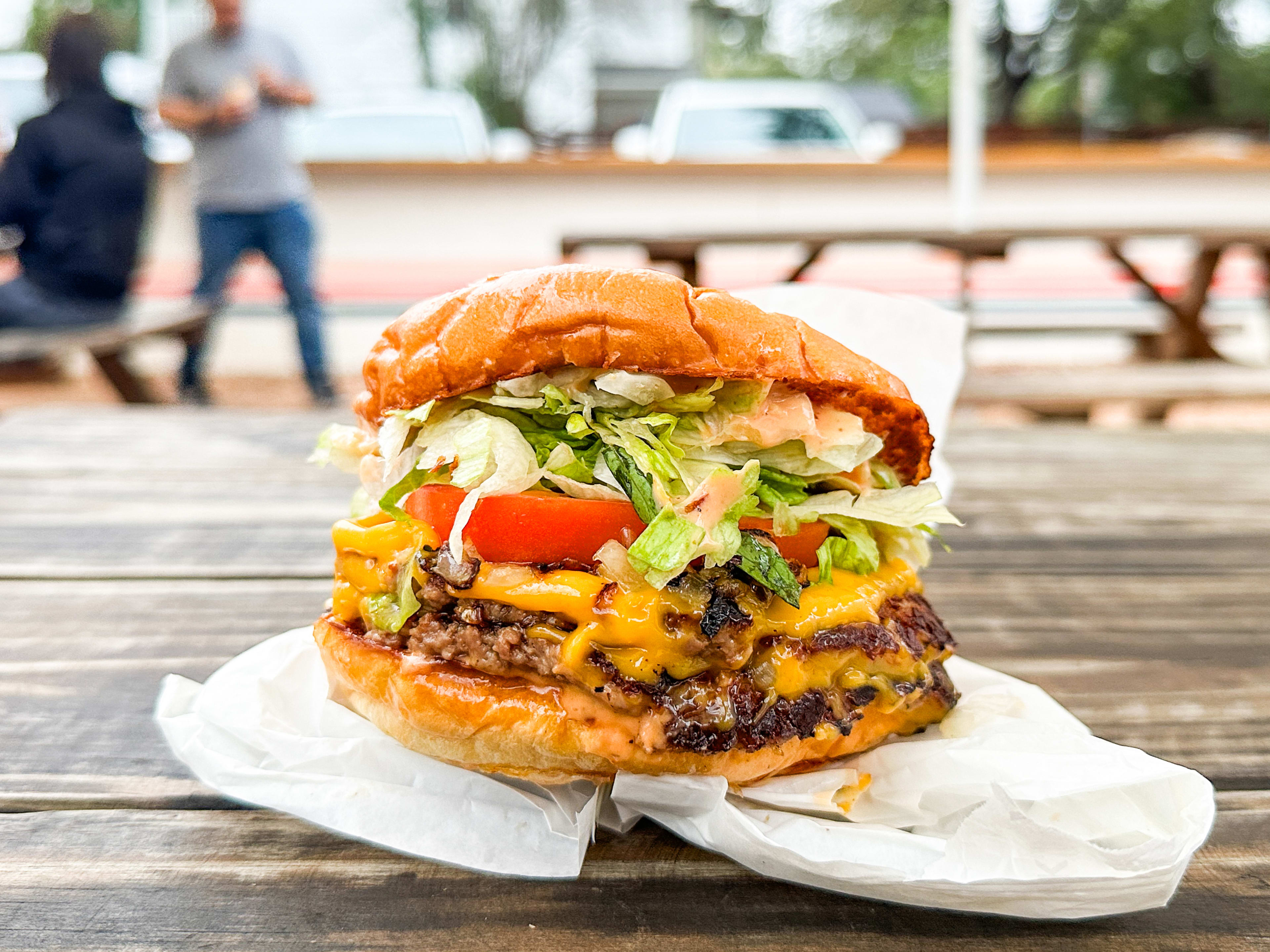 The Double Mission Burger sitting on a paper bag on top of a picnic table at Mission Burger.