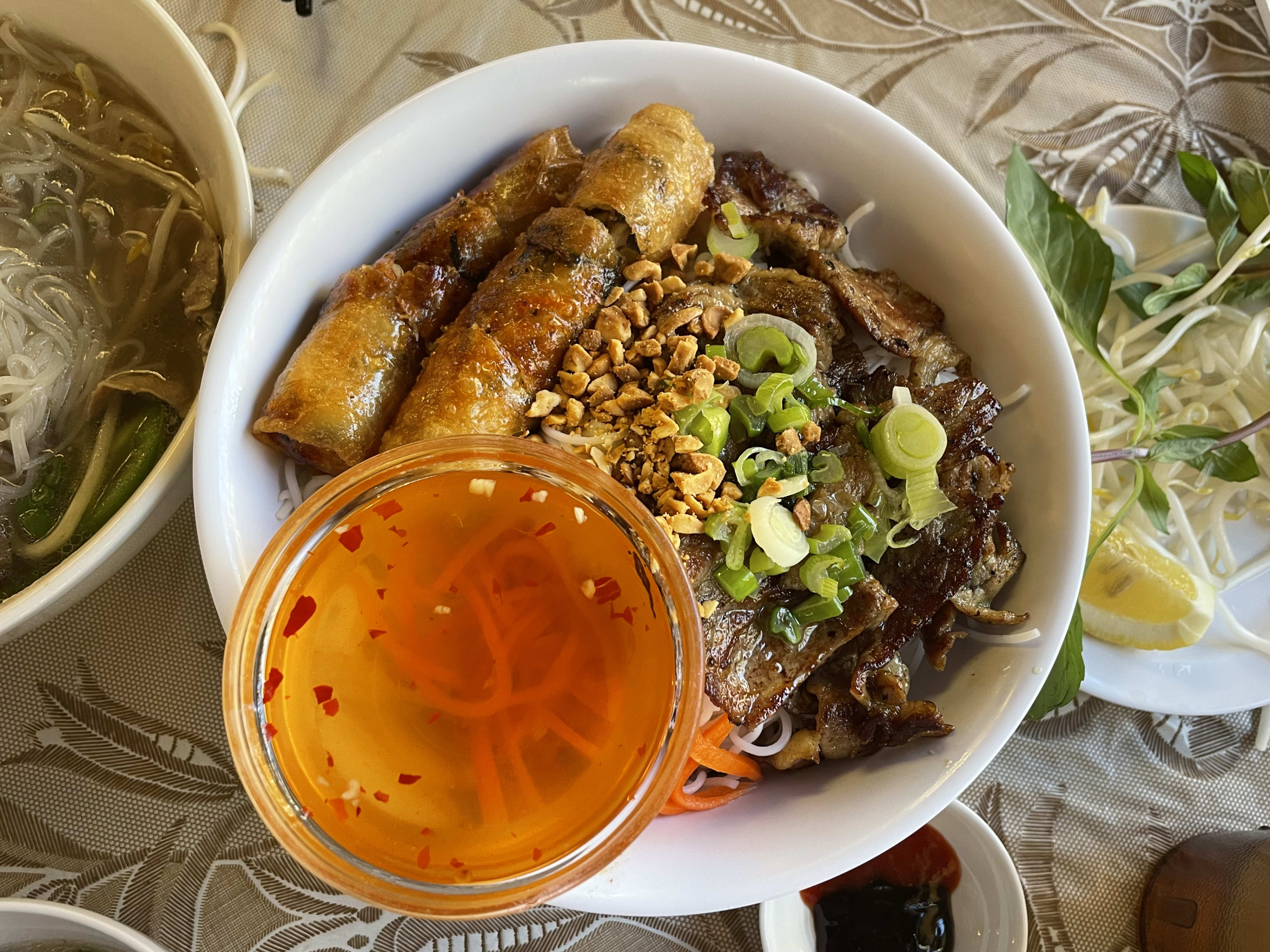 vermicelli noodle bowl with sauce in cup, eggrolls, meat and toppings