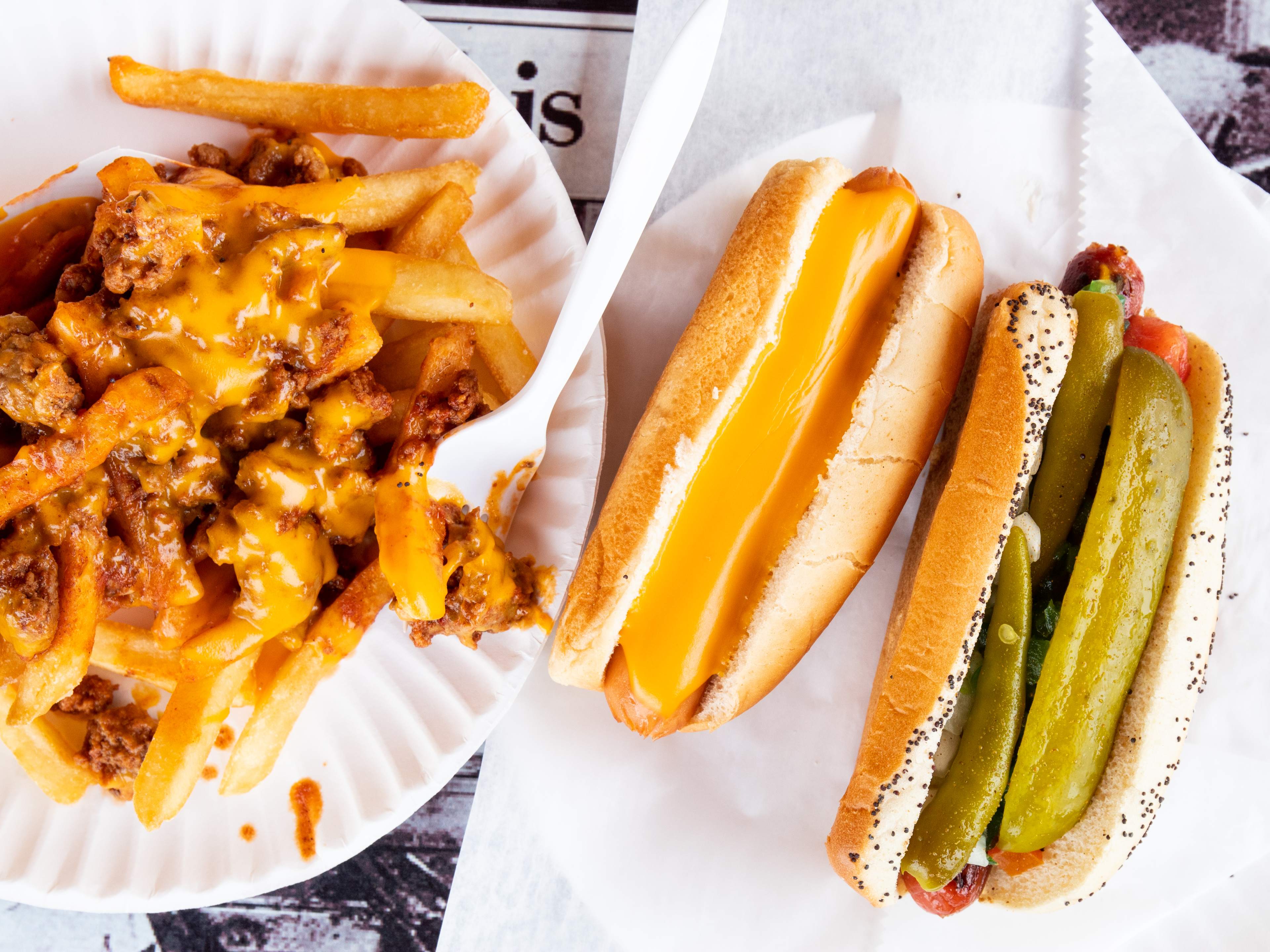 chicago style hot dogs with pickles and cheese sauce next to paper plate of chili cheese fries