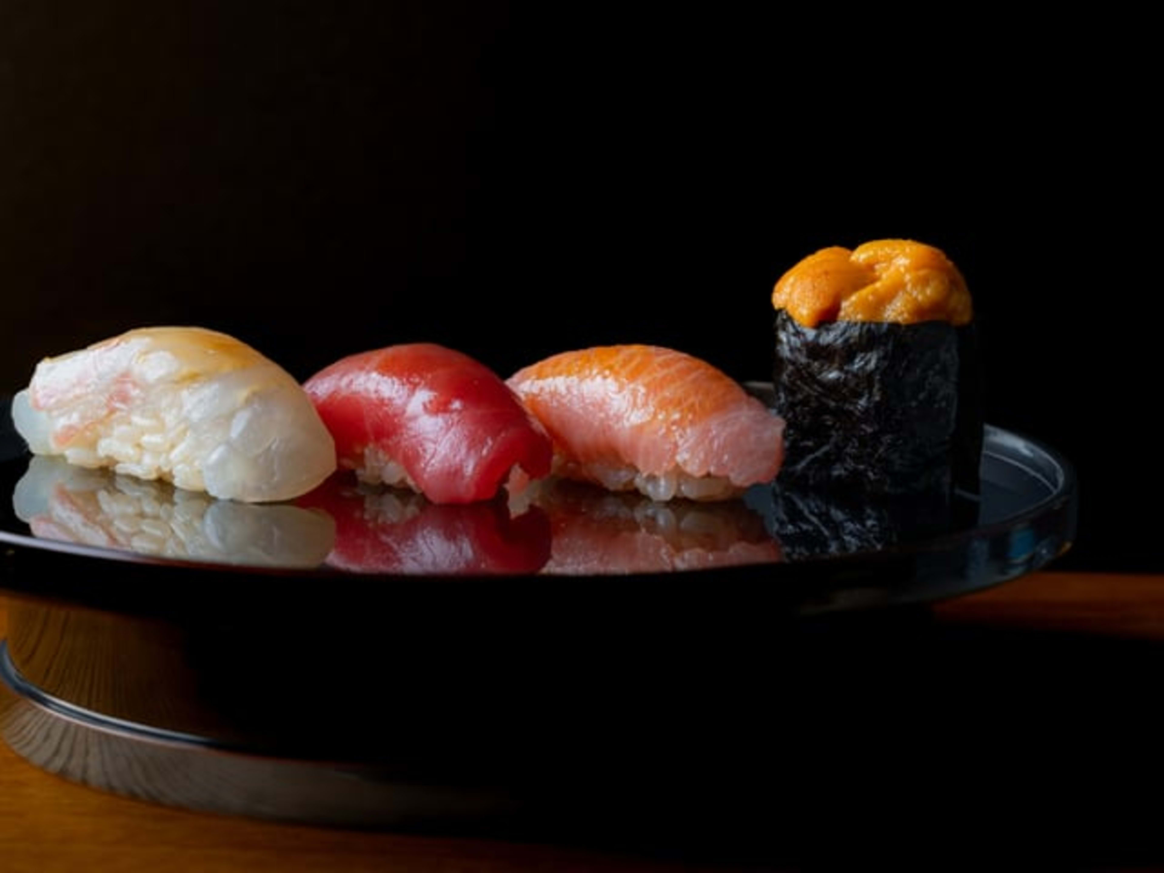 Four pieces of nigiri on a black platter.