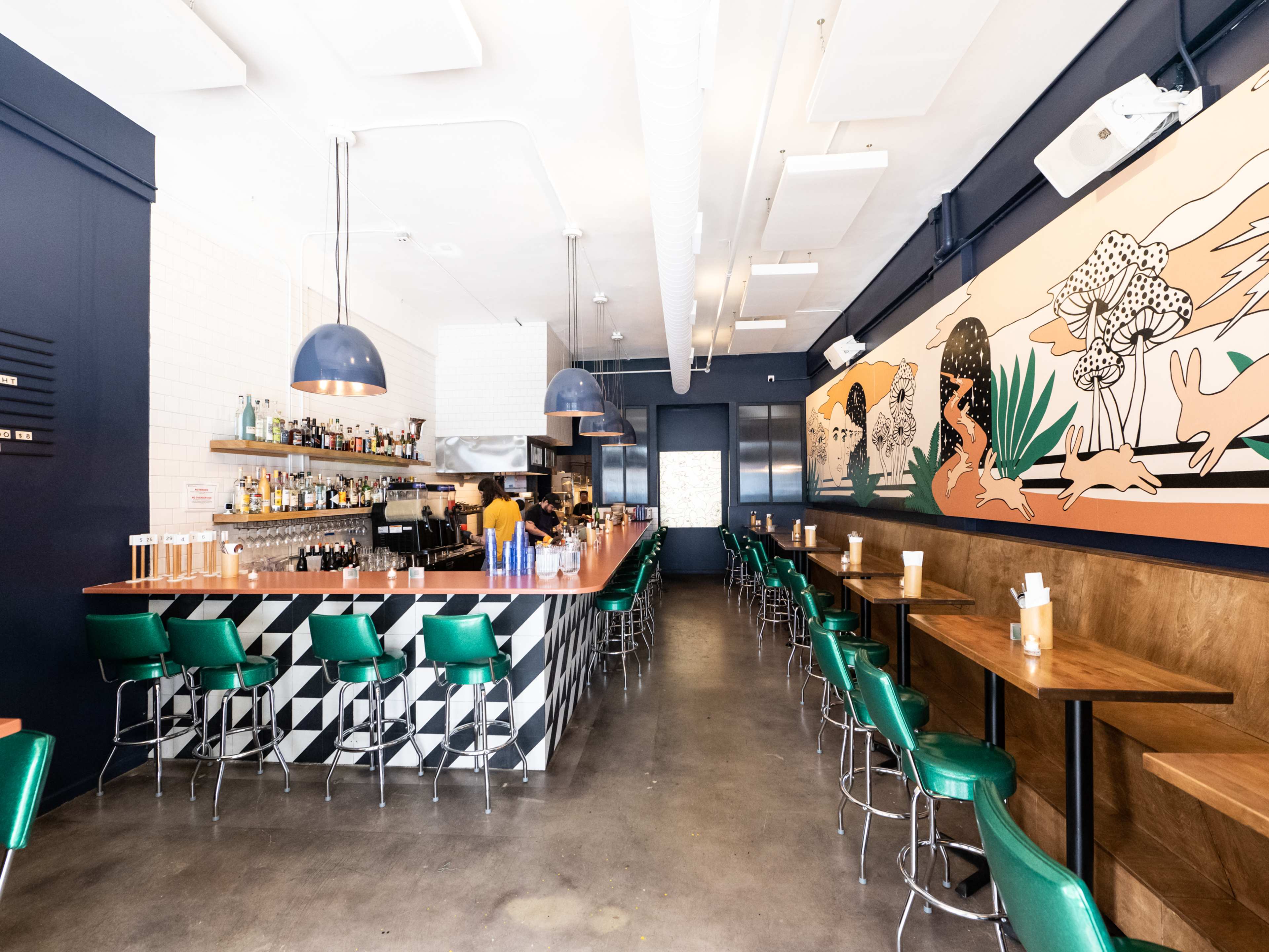 wine bar with an L-shaped bar, metallic green barstools, and a row of wooden tables