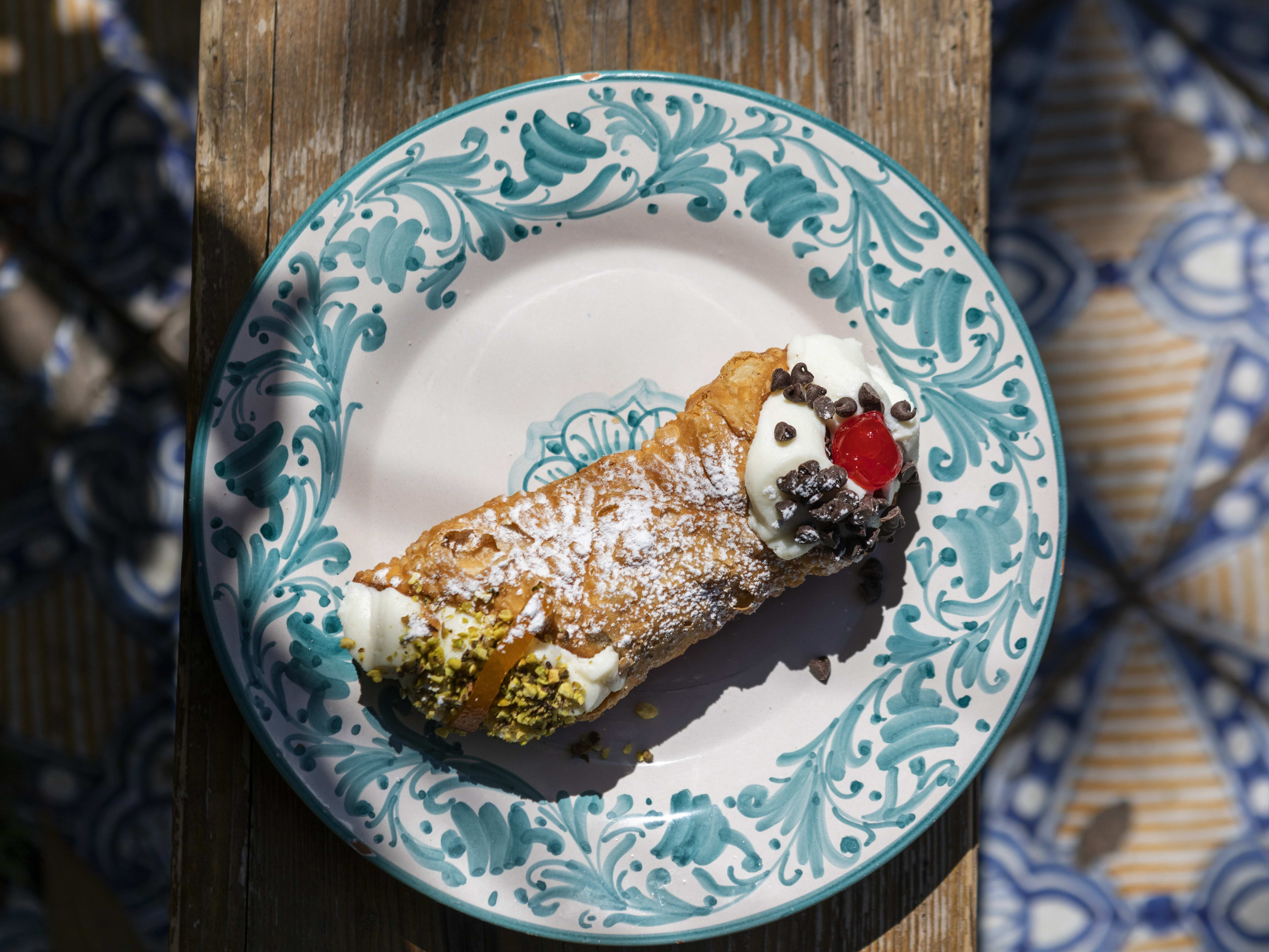 a cannolo on a decorative plate on a wooden table outside