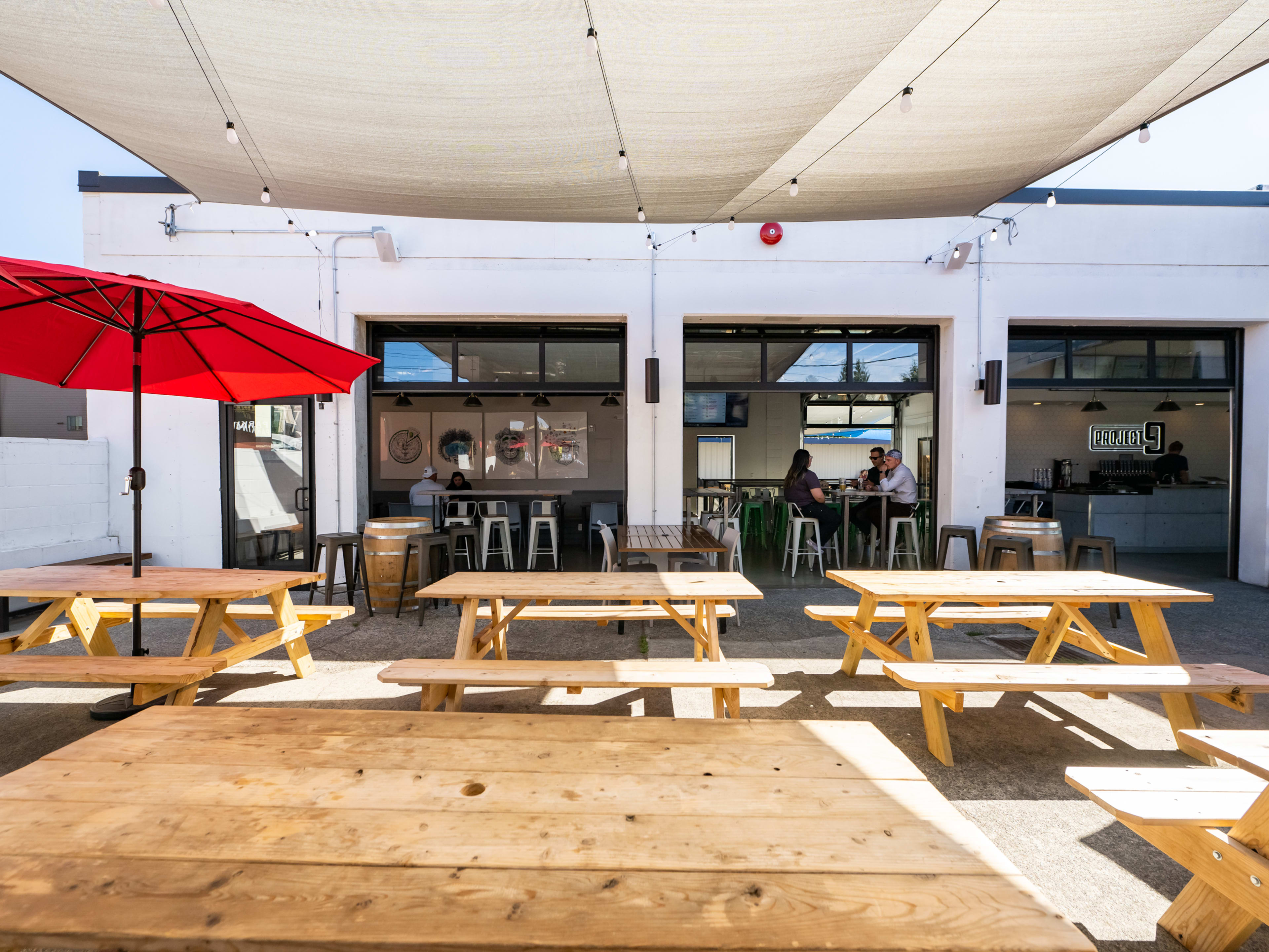 patio with wooden picnic tables and umbrellas, facing toward taproom with open garage doors