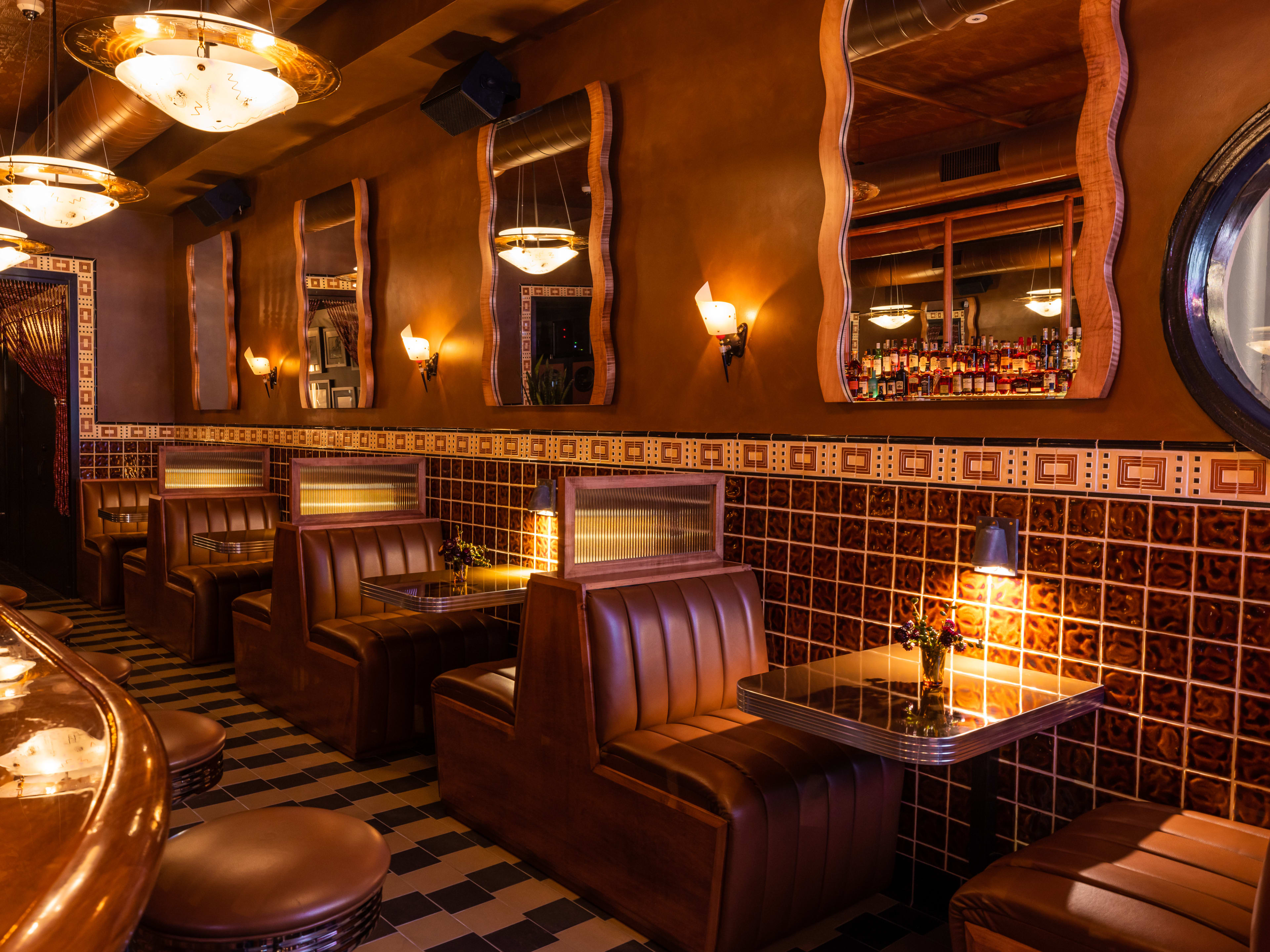 The brown hued interior of Bar Next Door. Small leather booths with tables are lined against the wall and a bar is to the left.