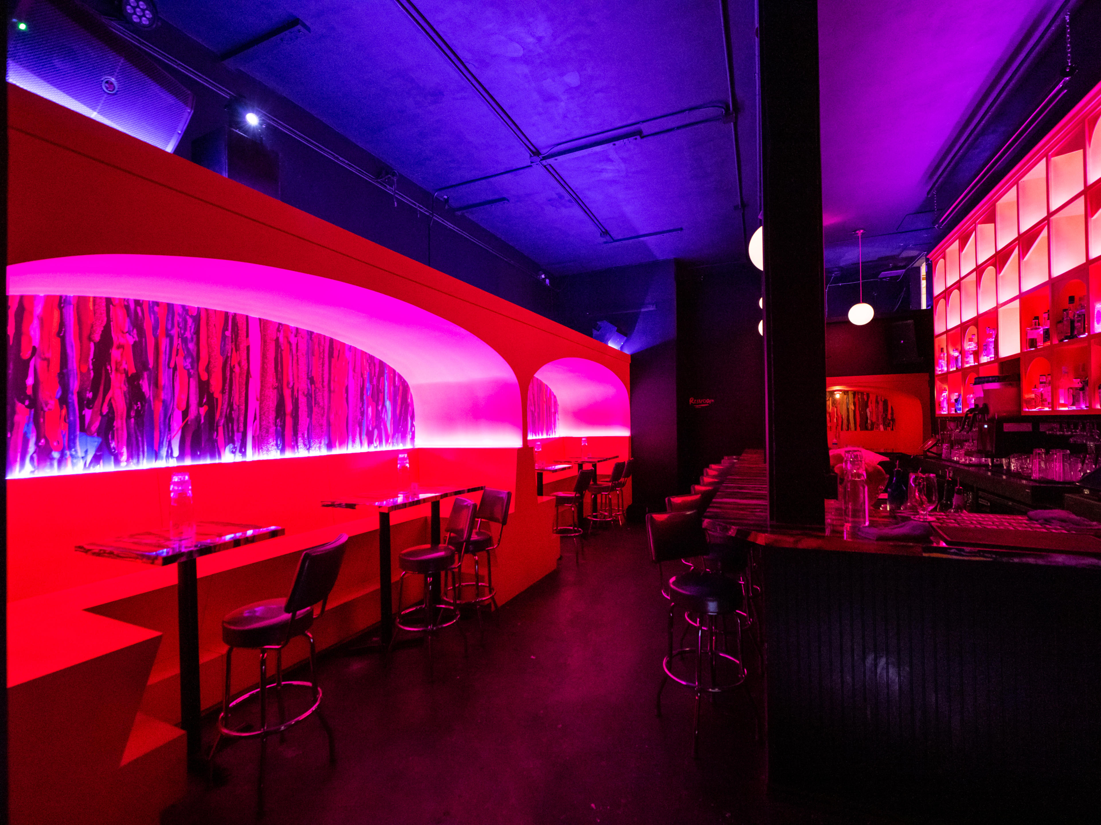 Dark bar with neon pink lighting and cavernous booths