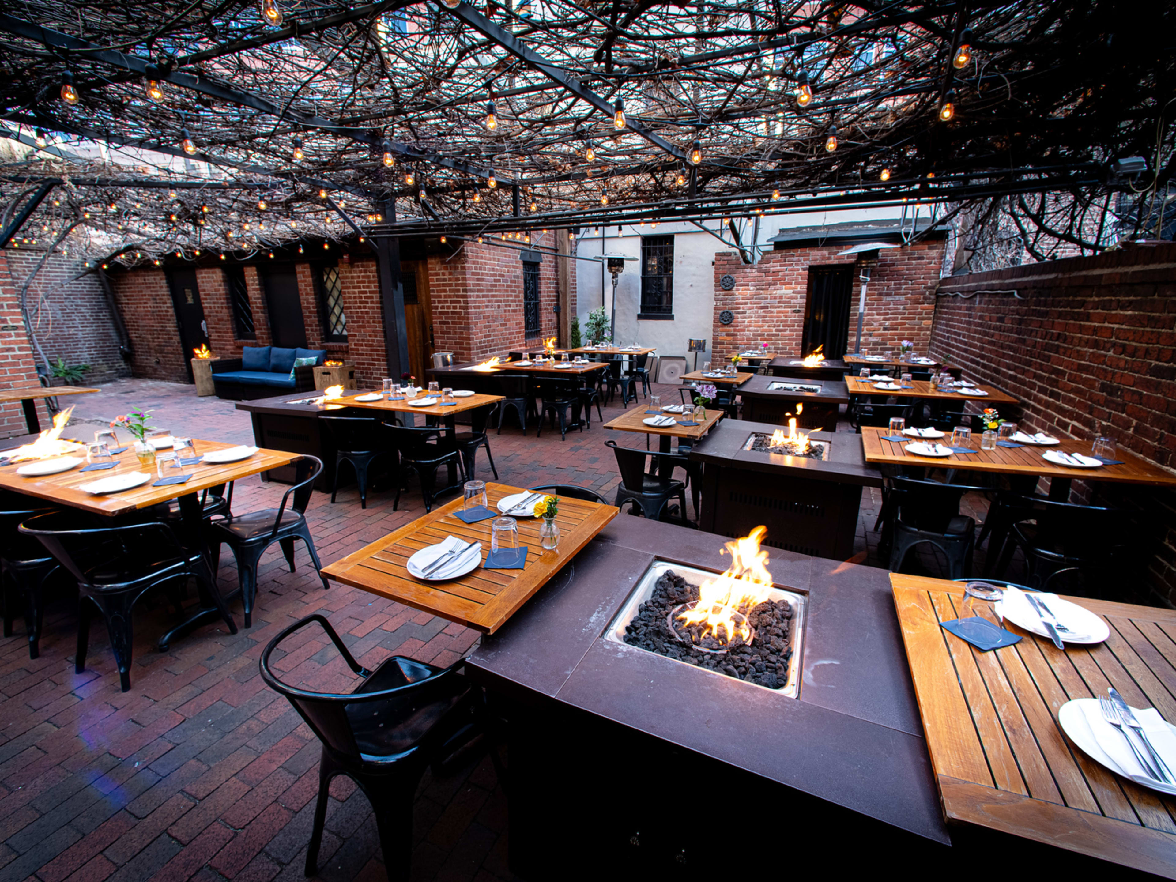 outdoor brick patio with fire pits between each table and twinkle lights