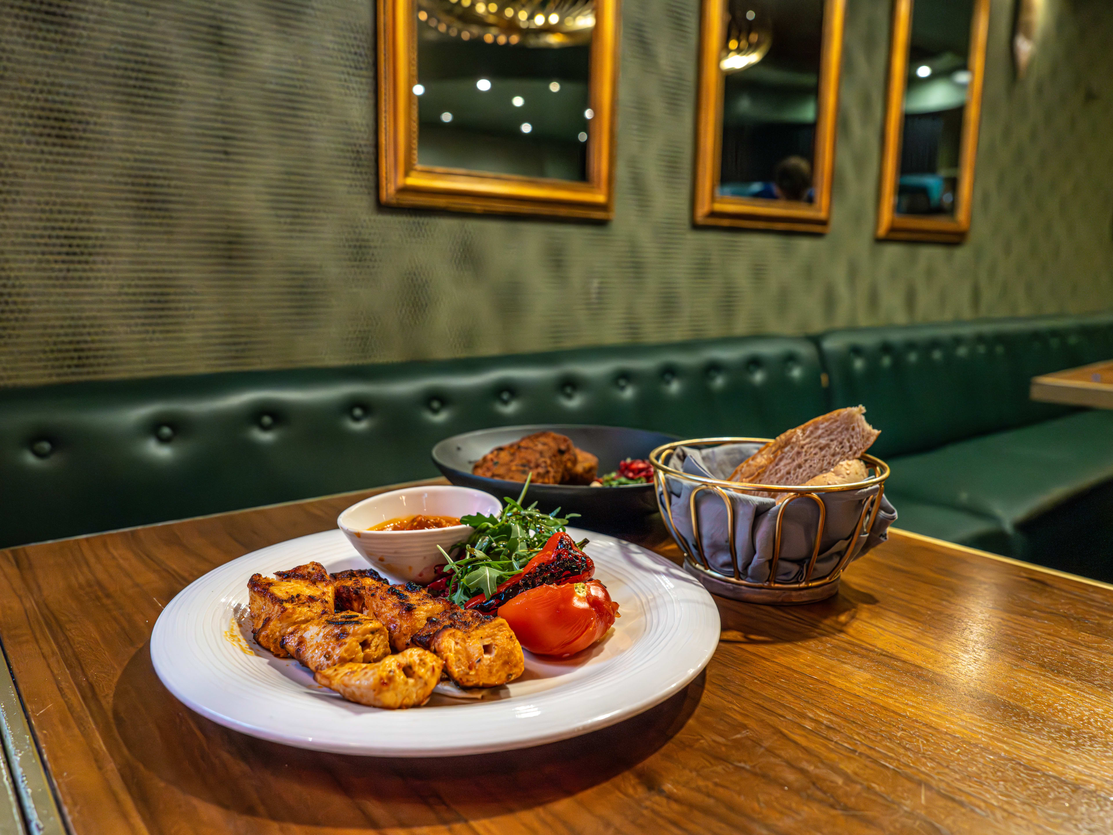 The falafel, bread, and sheesh plates from Ishtar on a wooden table next to a leather banquette.