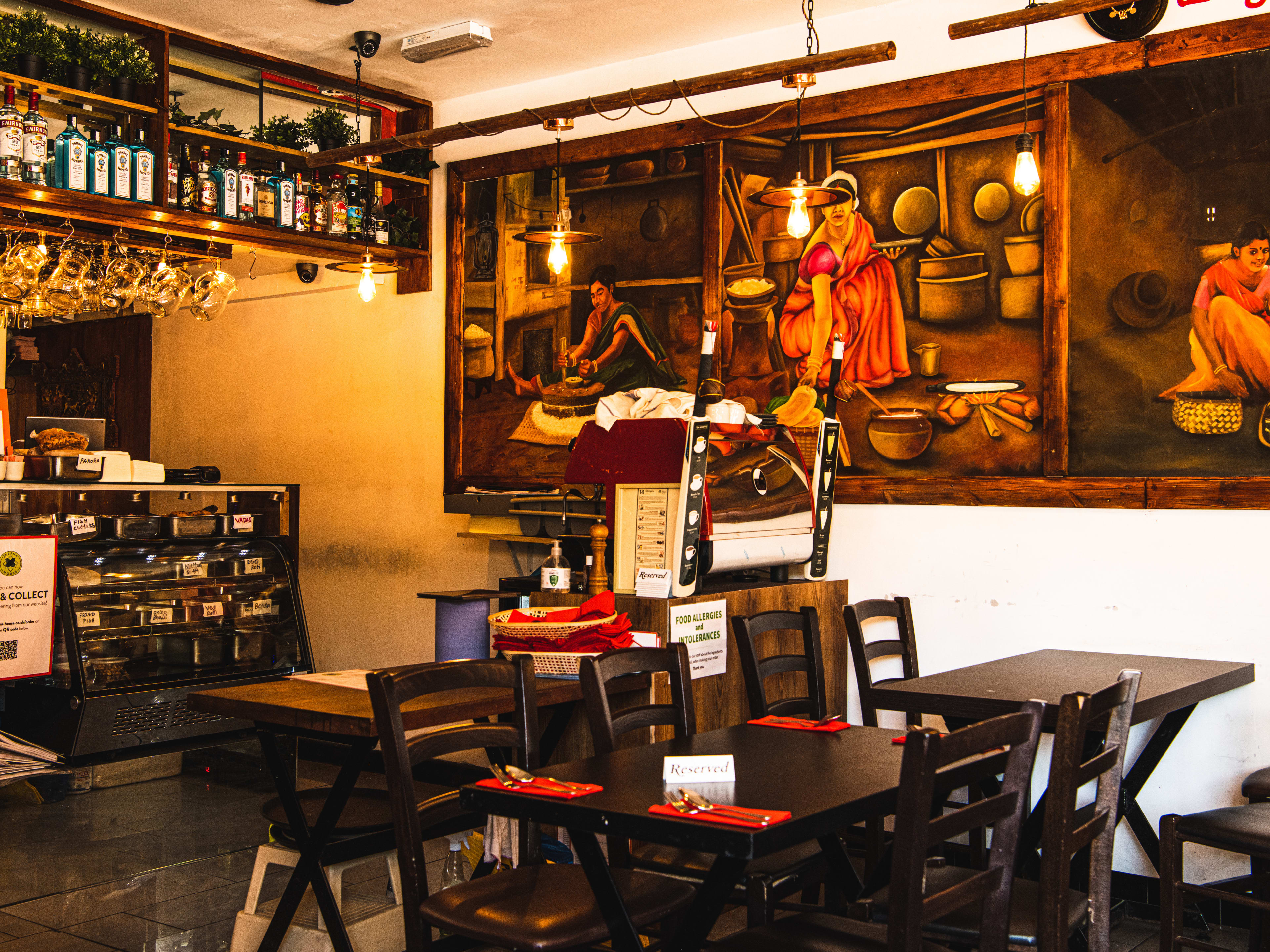 Restaurant interior with brown wooden tables and chairs, and paintings depicting women cooking on the walls.