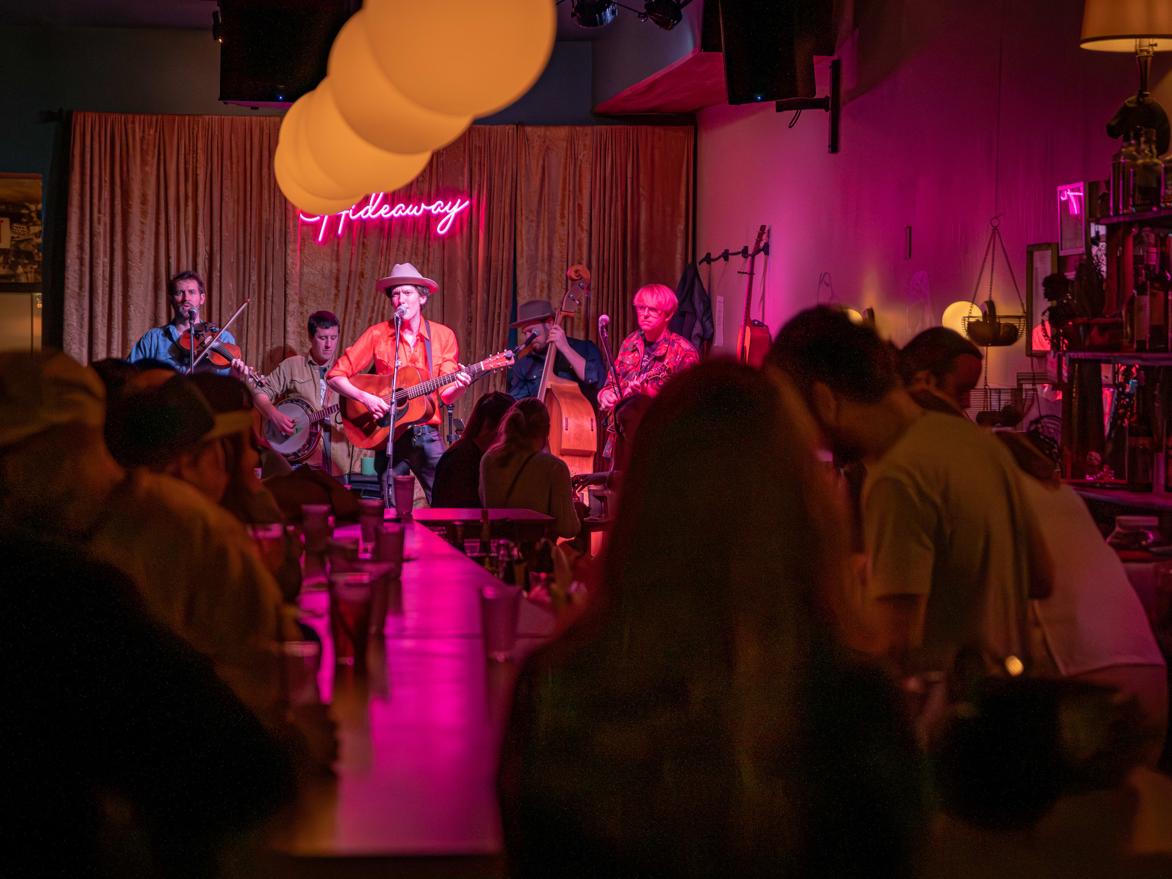 Band playing live set under pink neon lights for seated crowd at Jane's Hideaway