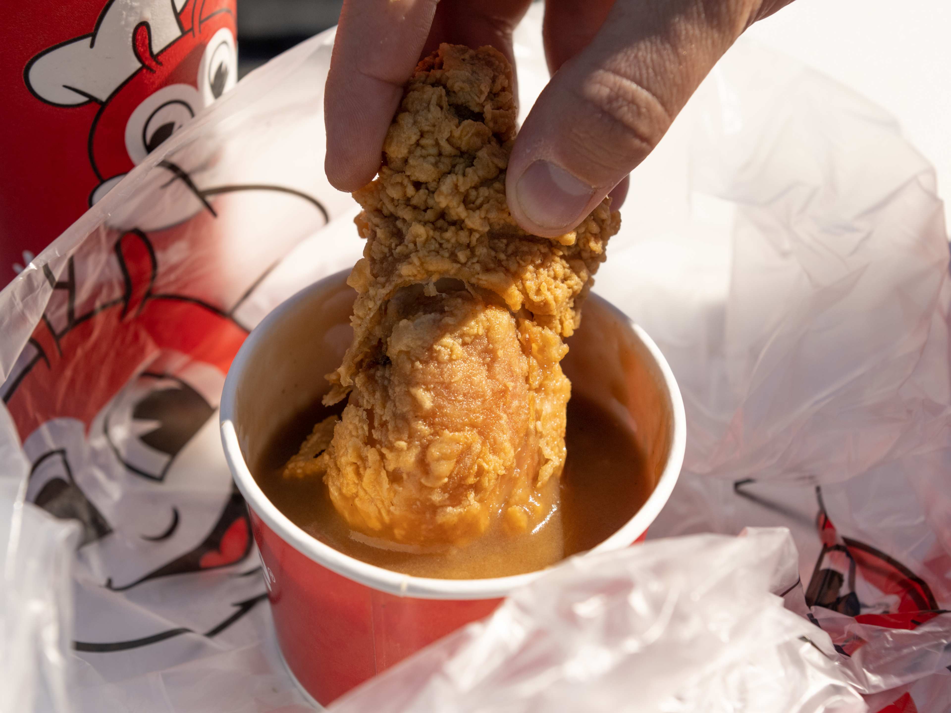 A person dipping fried chicken into gravy from Jollibee.