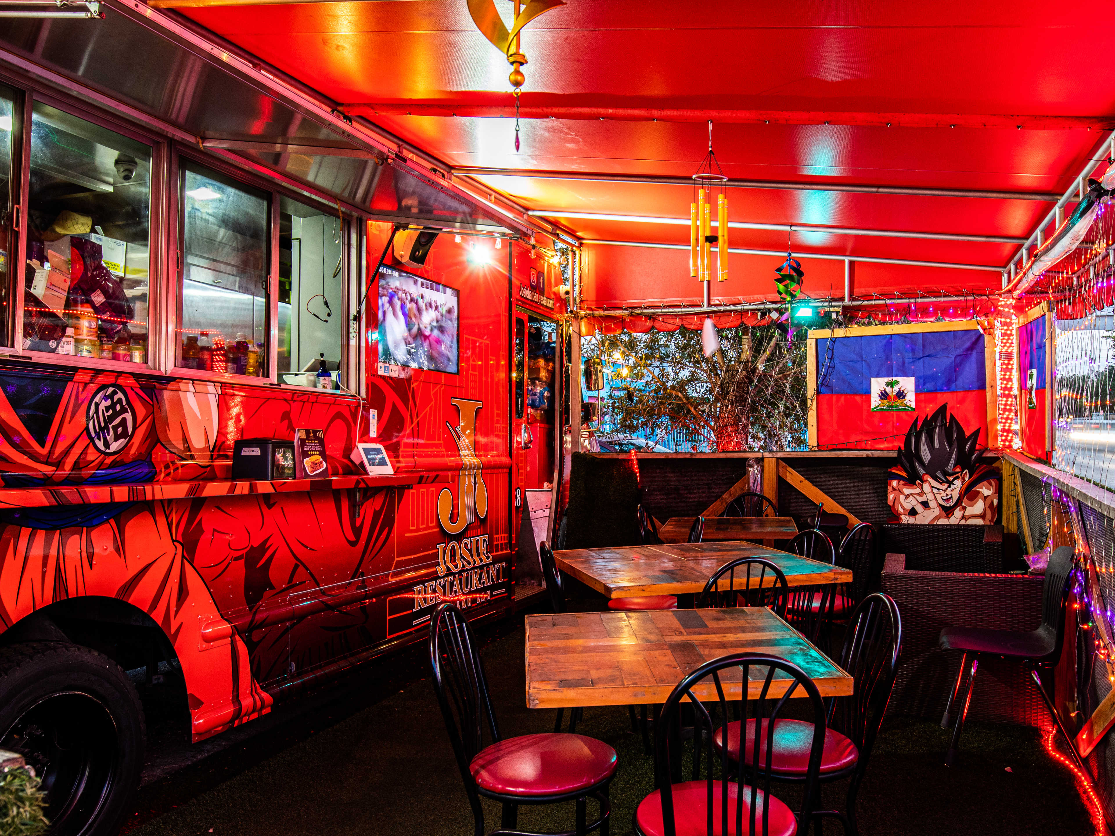 A red food truck with some chairs and an awning in front of it.