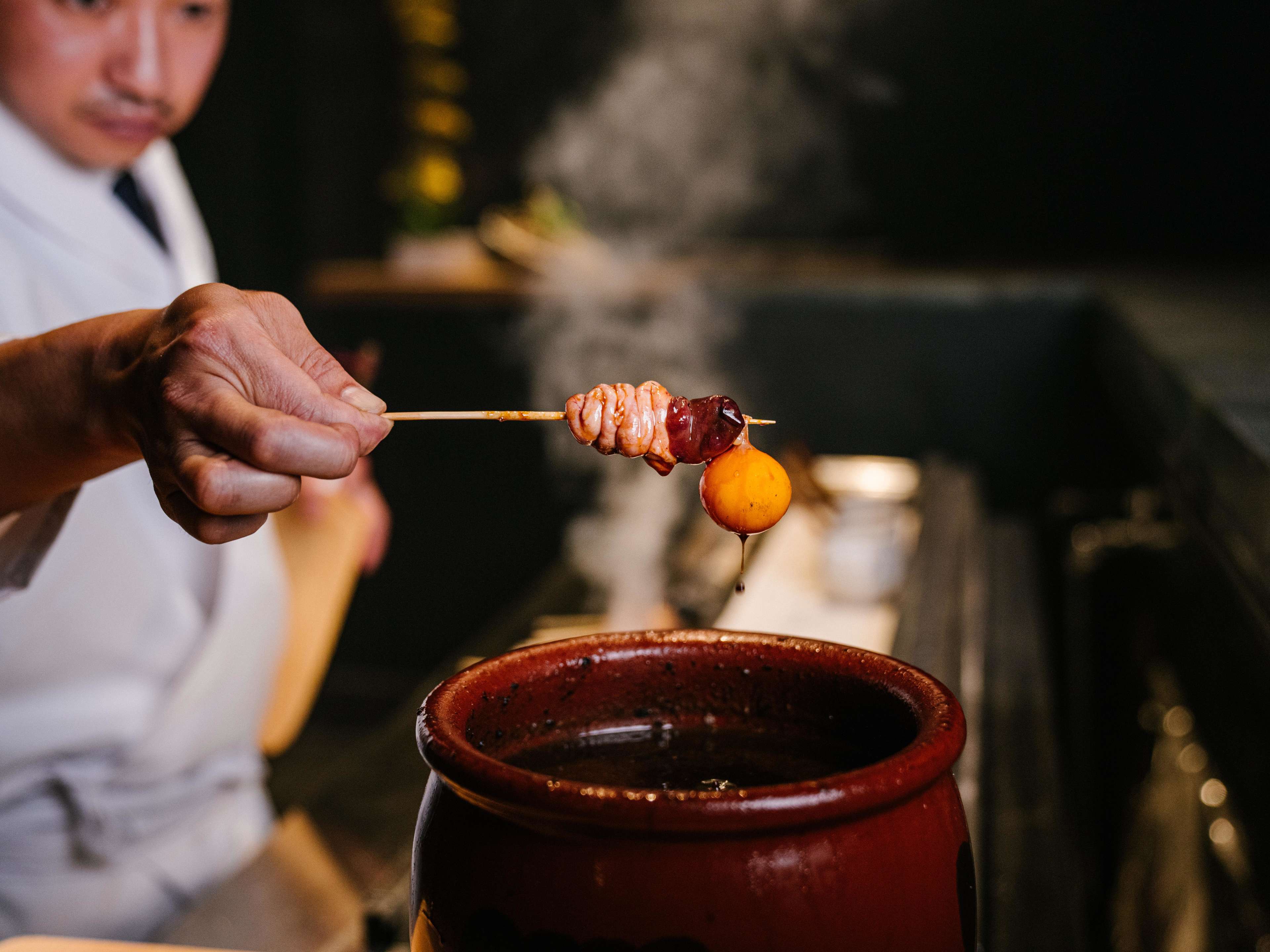 a yakitori skewer being dipped into a pot of tare