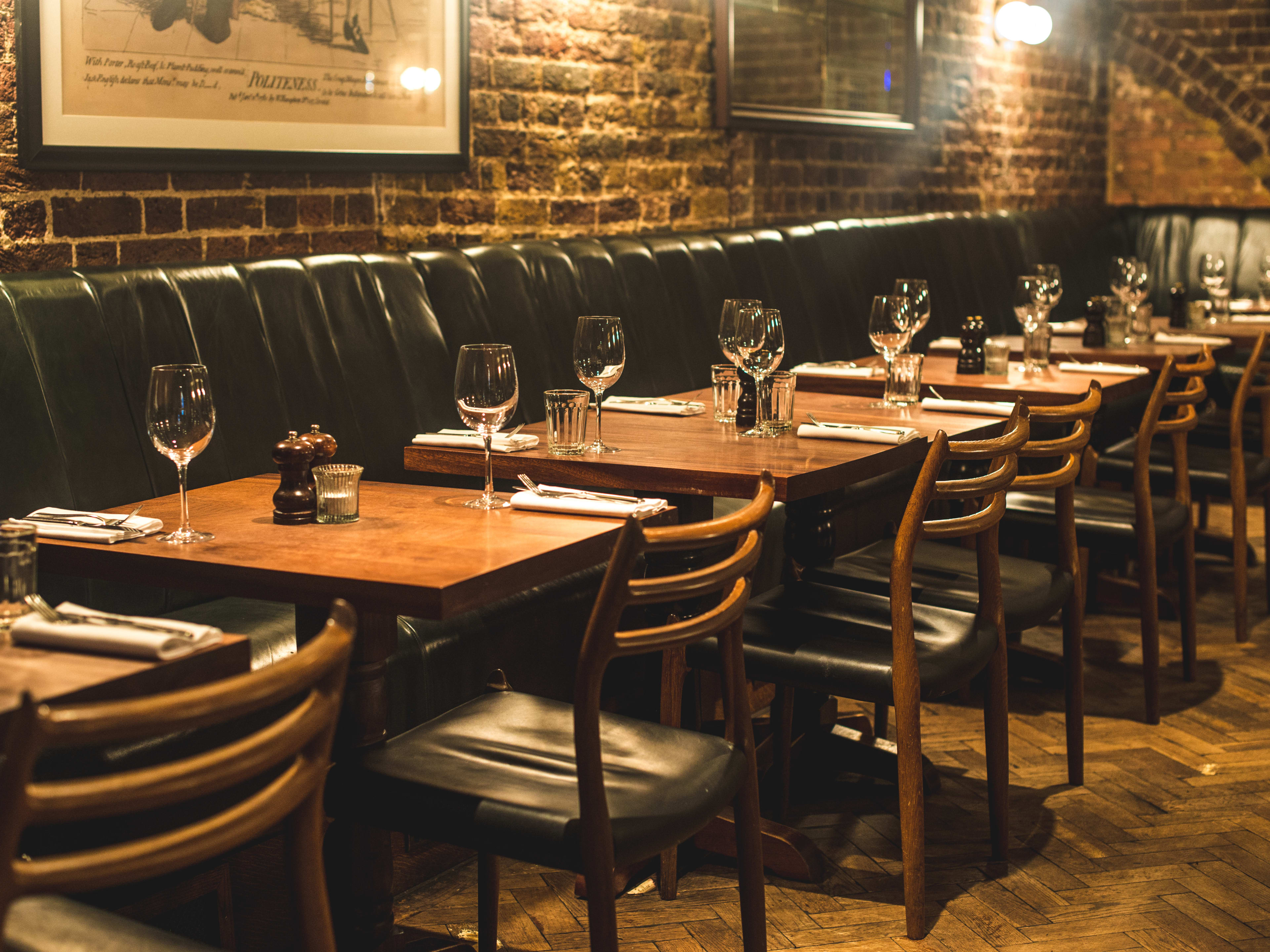 Dark green booths with two person tables line the brick interior of Hawksmoor Spitalfields.