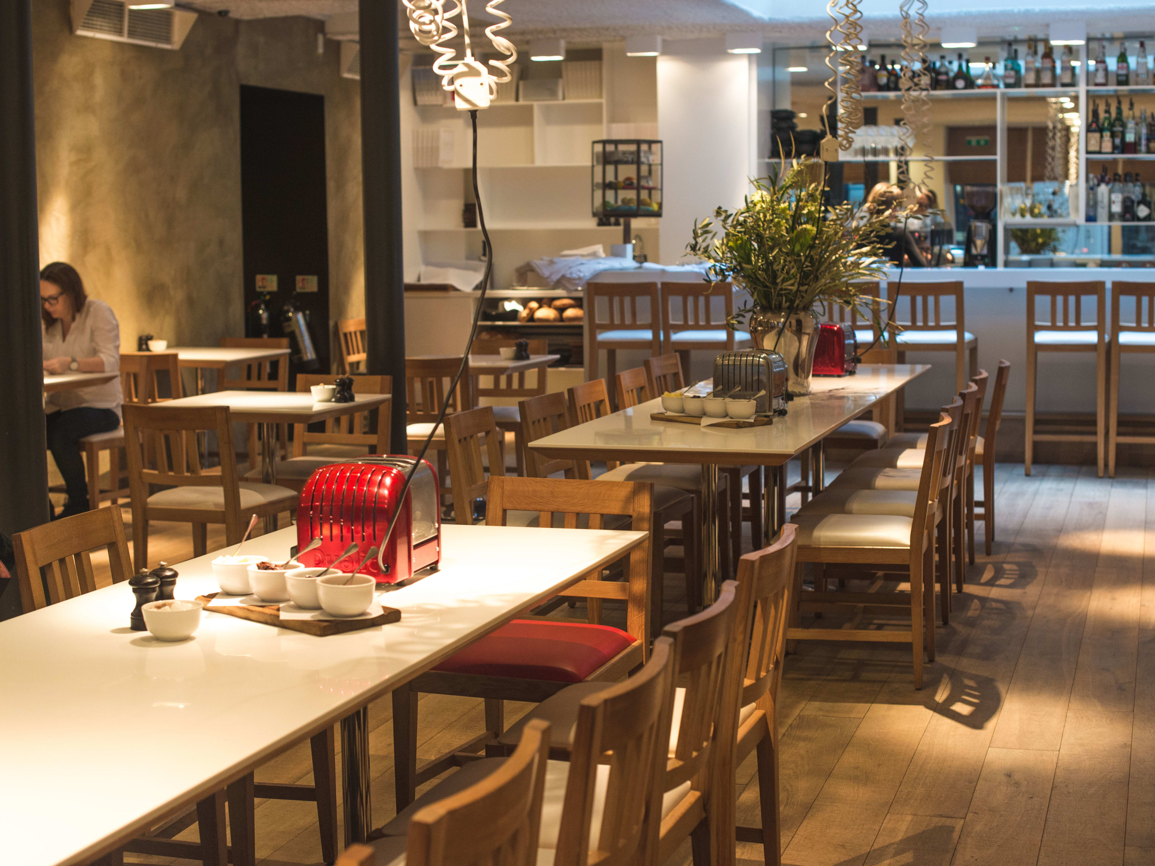 The interior of Ottolenghi Spitalfields. With long tables, a bar, a person sitting at a side table and personal toasters at every table.