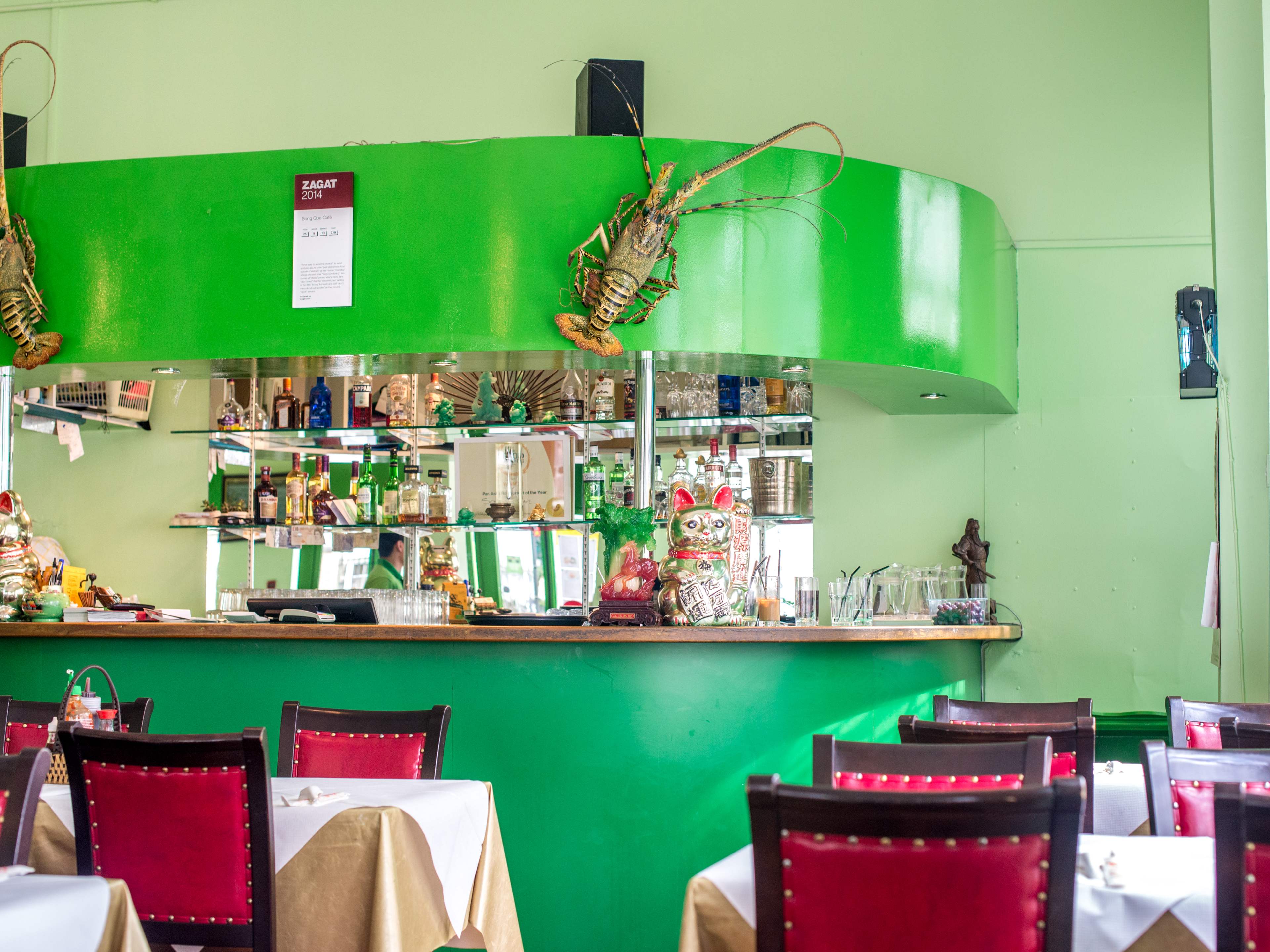 The green interior of Sông Quê. Two lobster sculptures hang on the top of the bar. There are tables with red leather and wooden chairs.