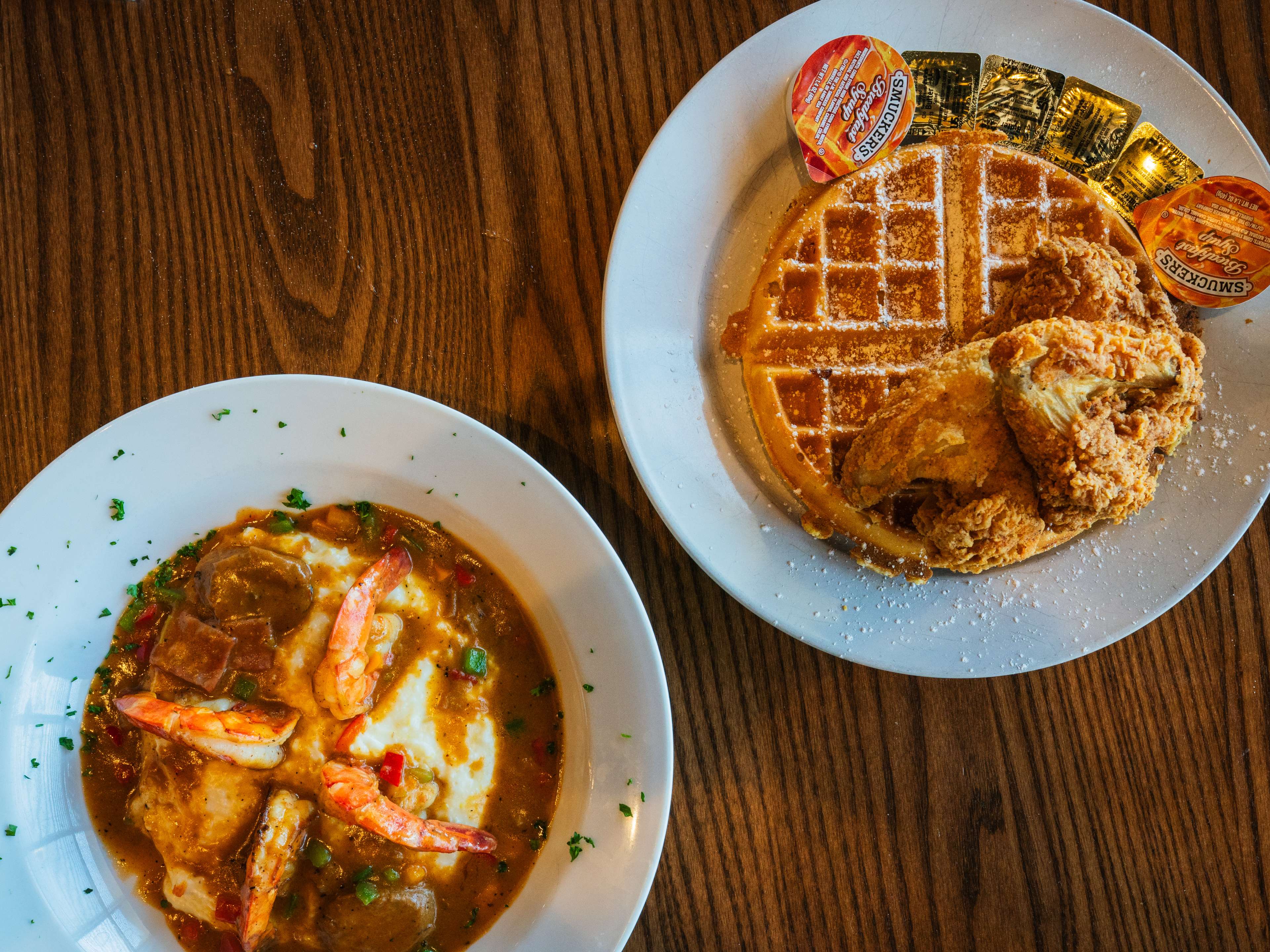 Overhead shot of chicken and waffles and shrimp and grits on a wooden table.