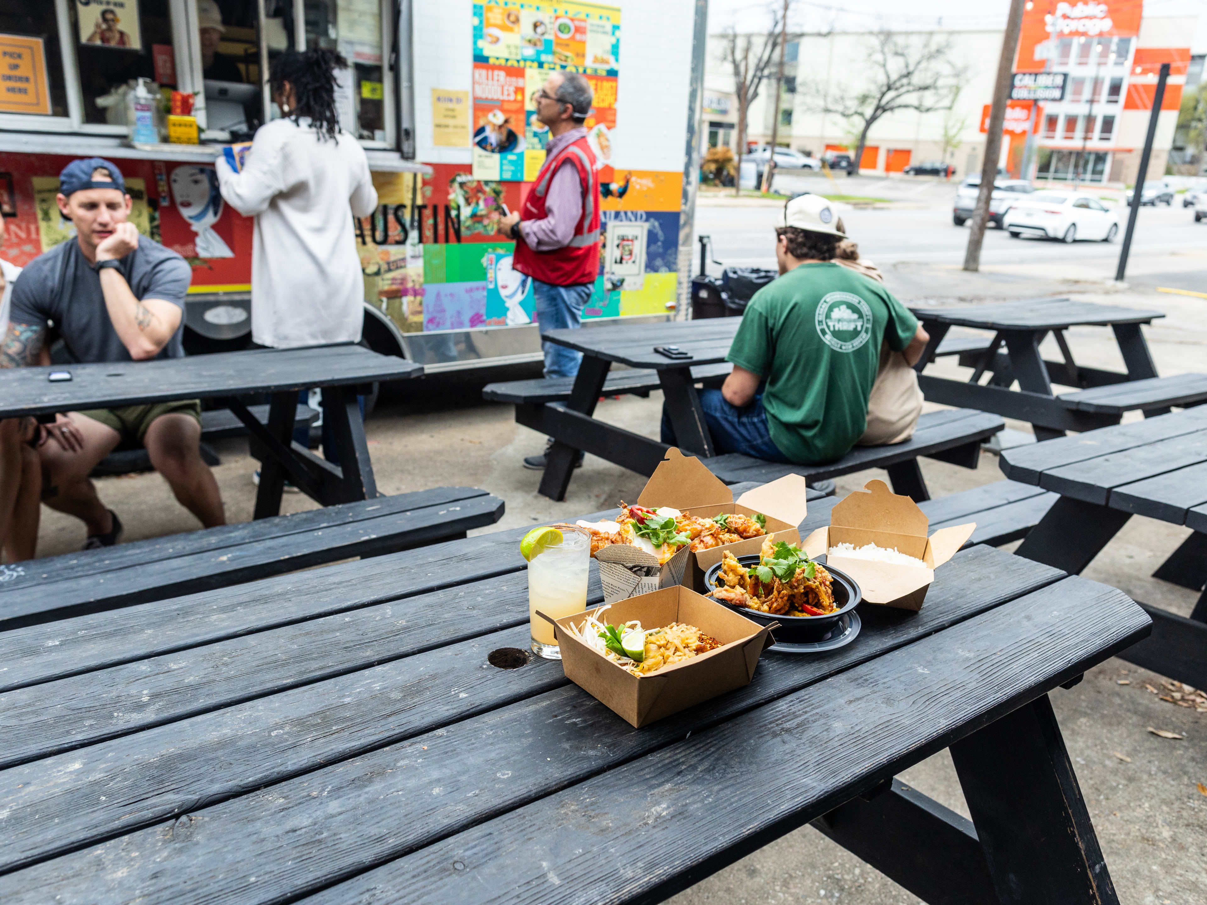 Thai food sitting in takeout containers on a picnic table outside