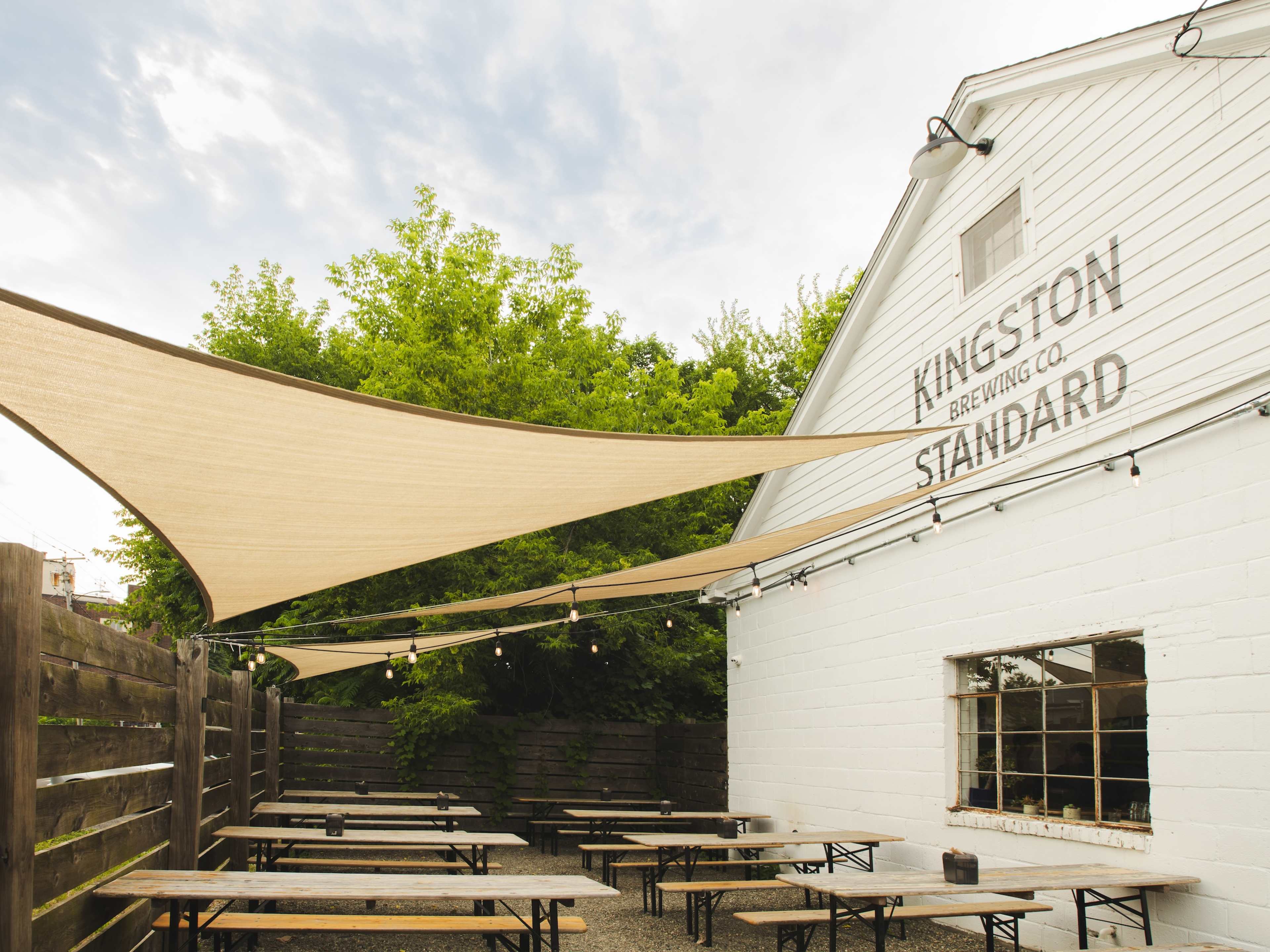 The white barn exterior of Kingston Standard brewery with picnic tables and a sun shade