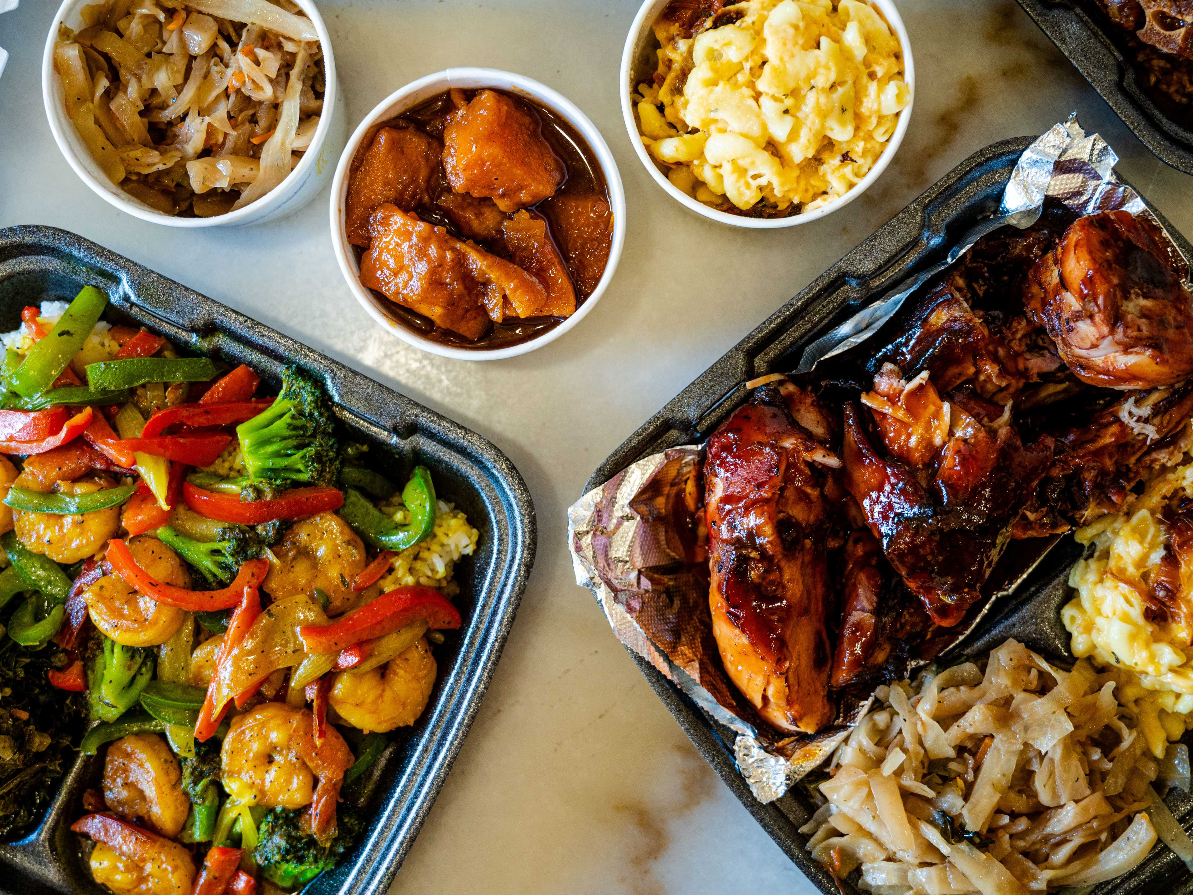 spread of takeout plates of wings, shrimp, veggies, mac and cheese, and yams