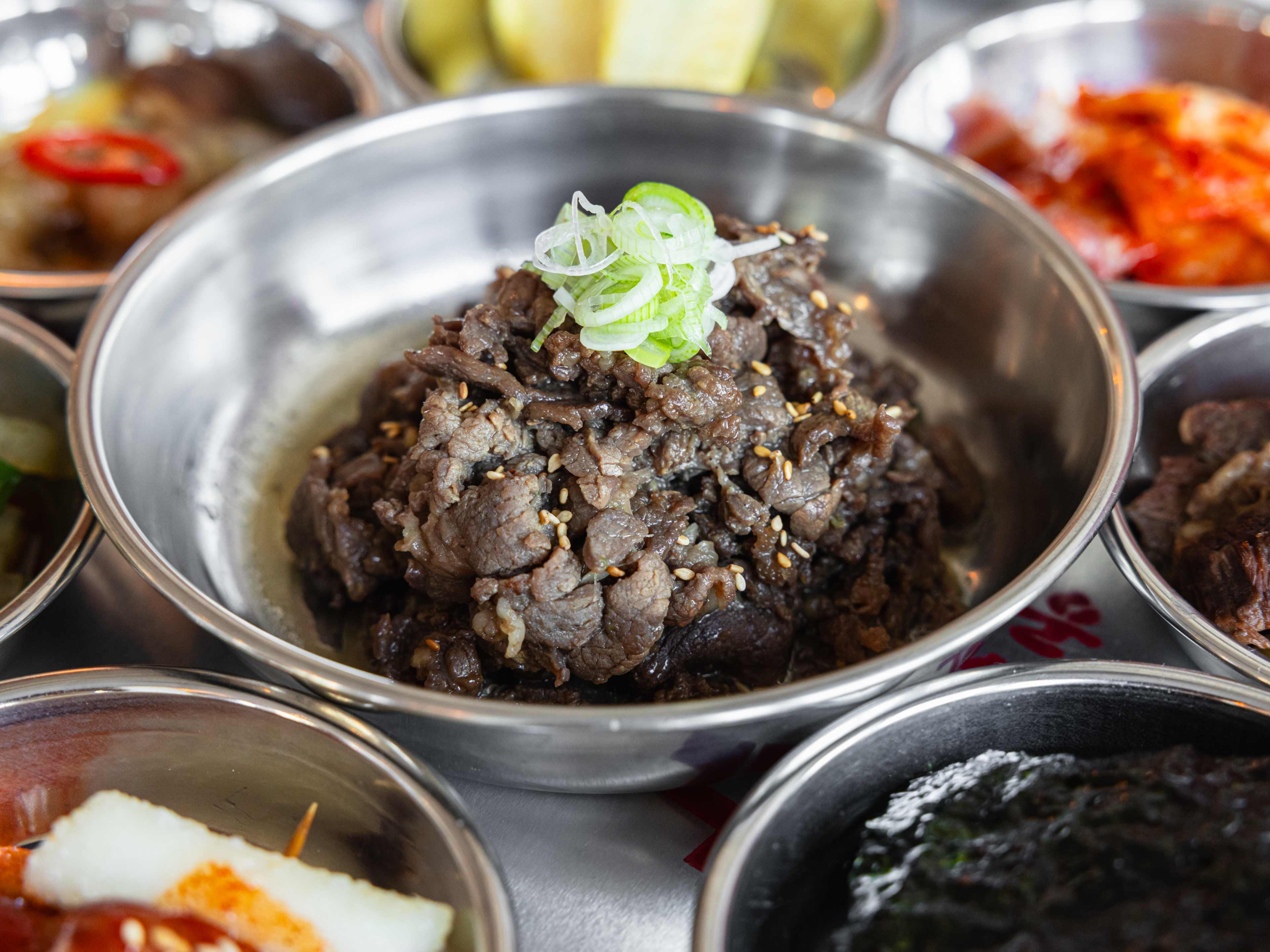 A small bowl of bulgogi surrounded by various sides.