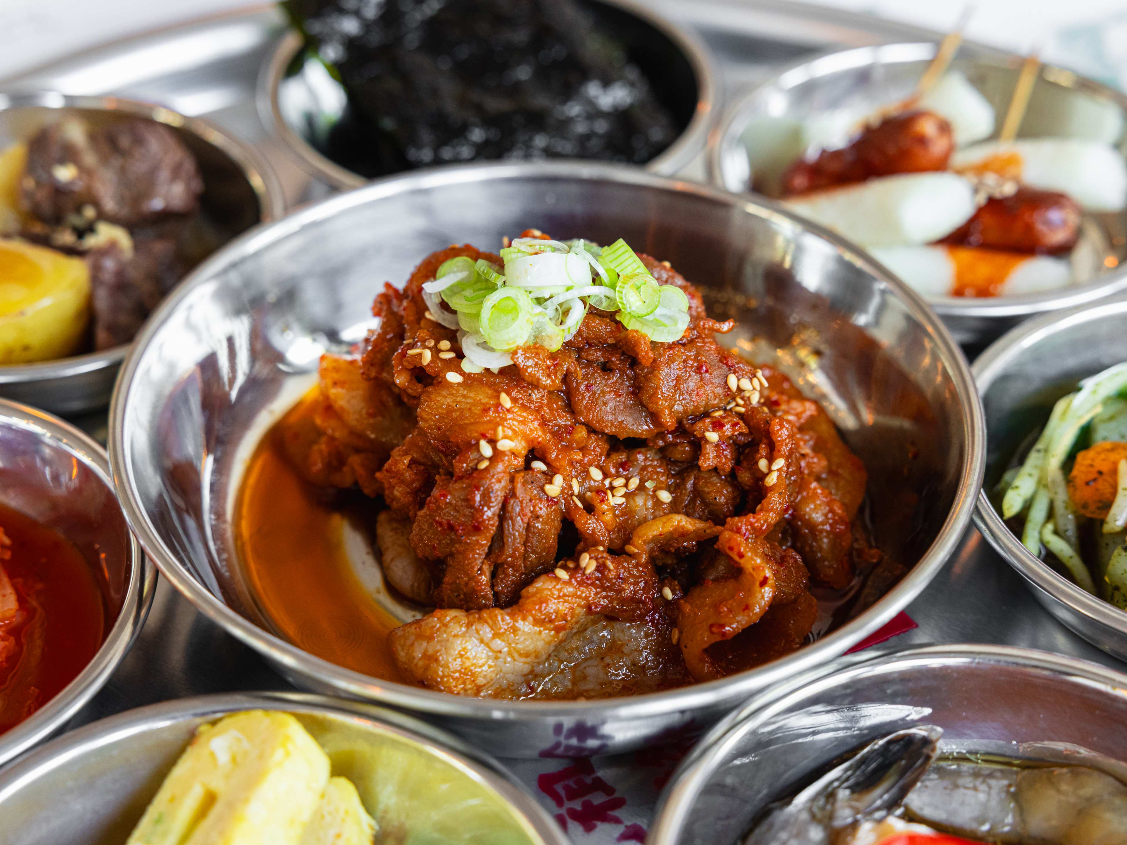 A small pile of spicy pork in a metal bowl surrounded by various sides.