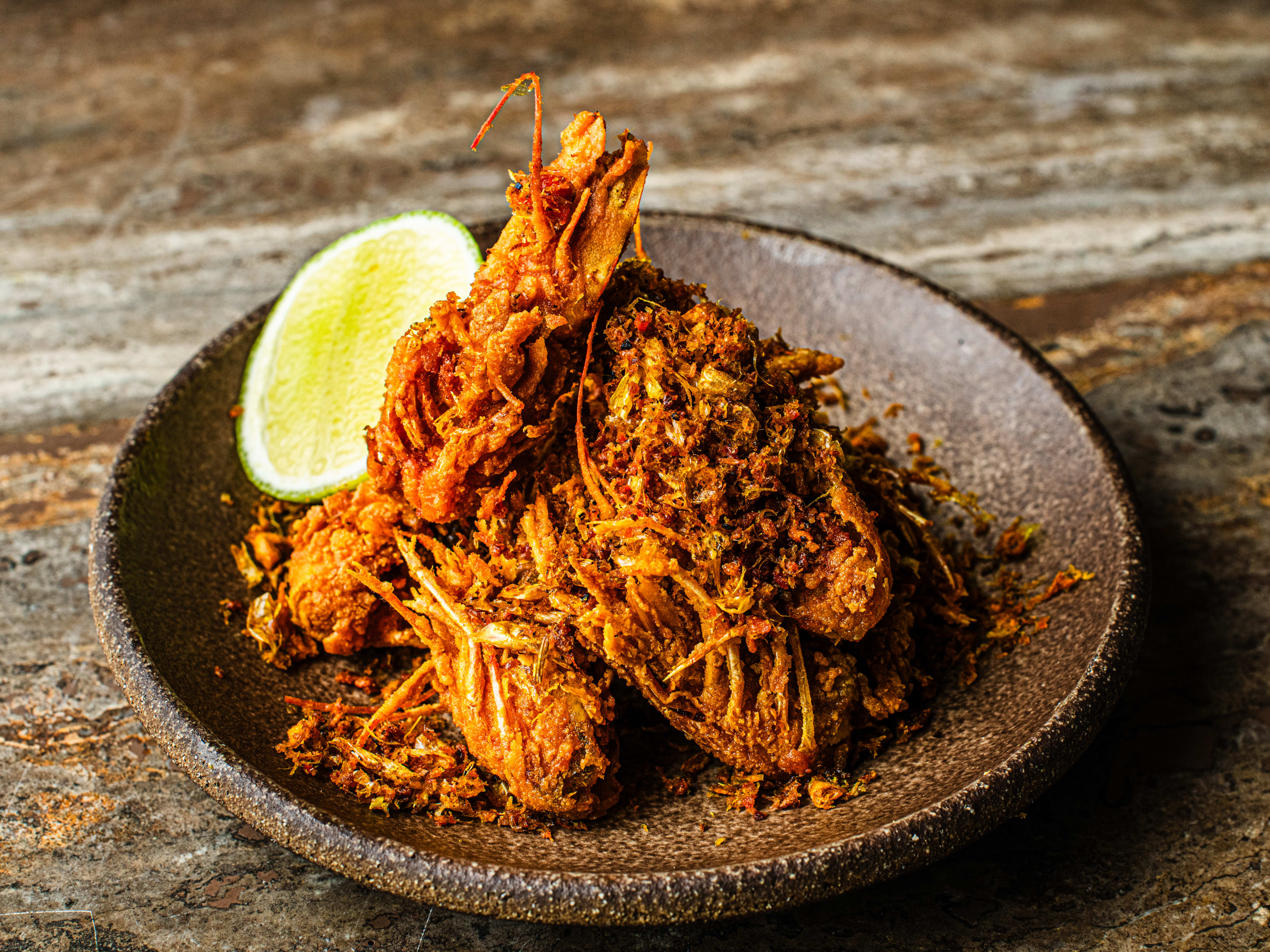 A plate of crispy prawn heads and a lime slice on a grey ceramic plate.