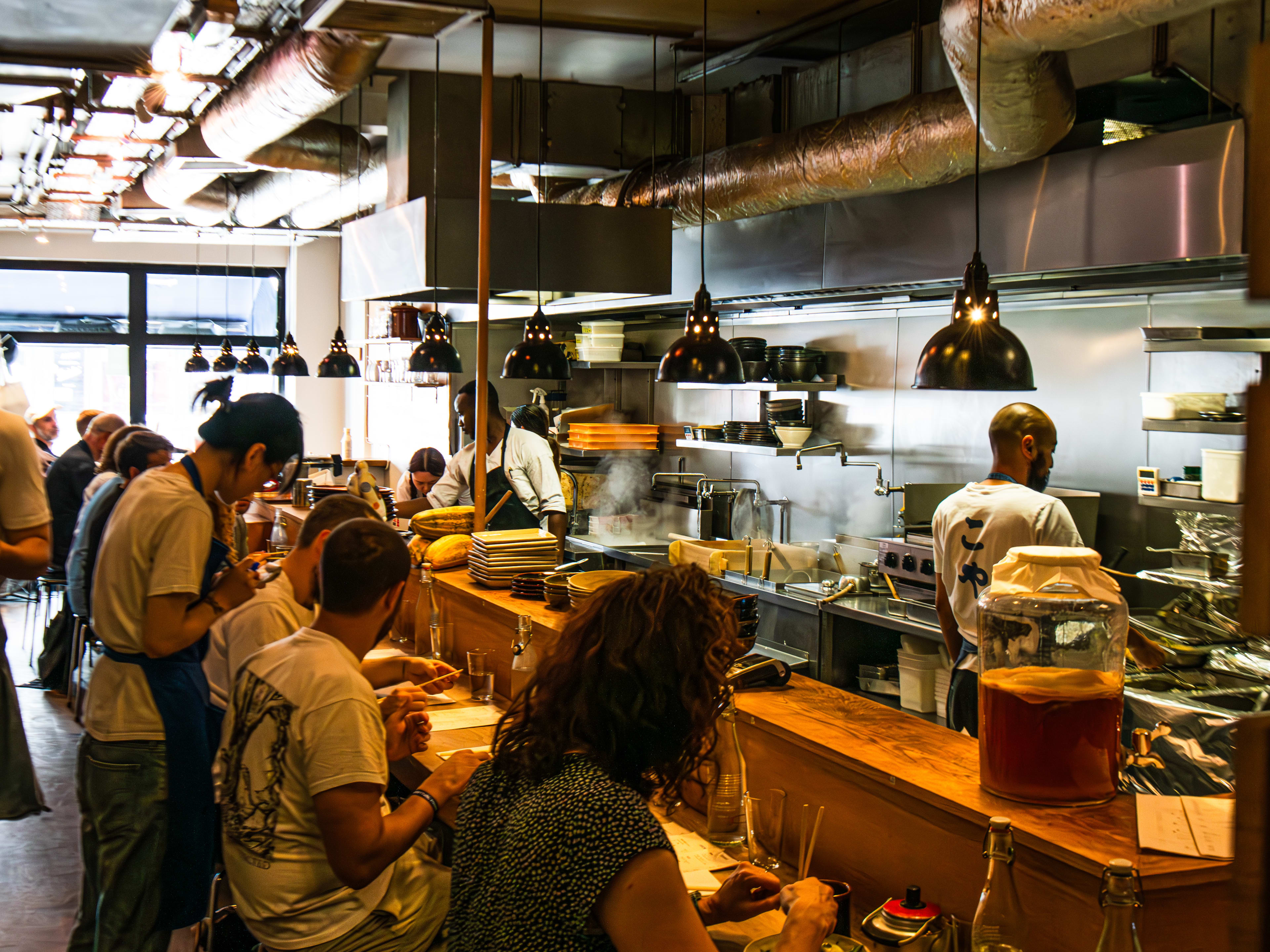 People dine at the bar at Koya Soho. Chefs are seen cooking in the kitchen behind the bar.