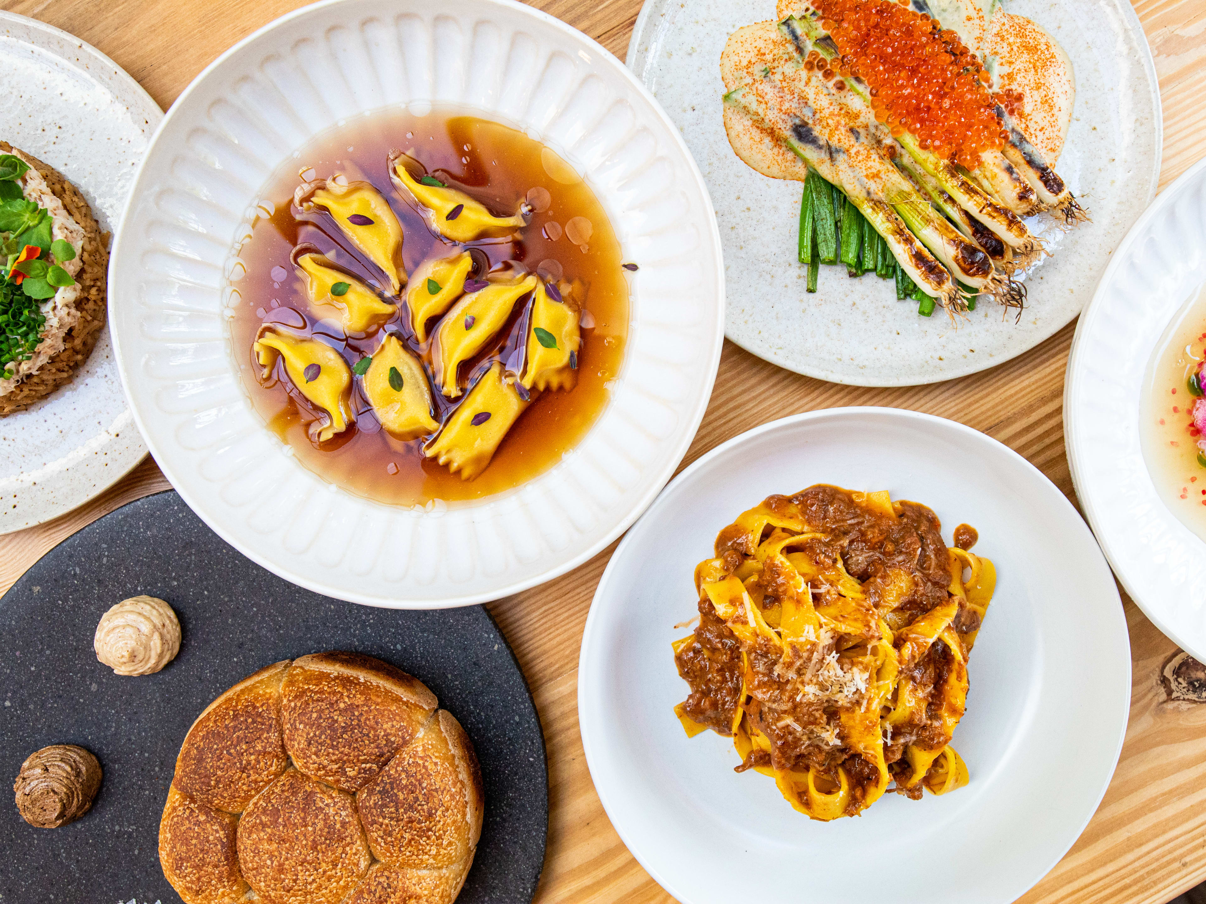 spread of dishes such as pastas, bread, veg, and crudo