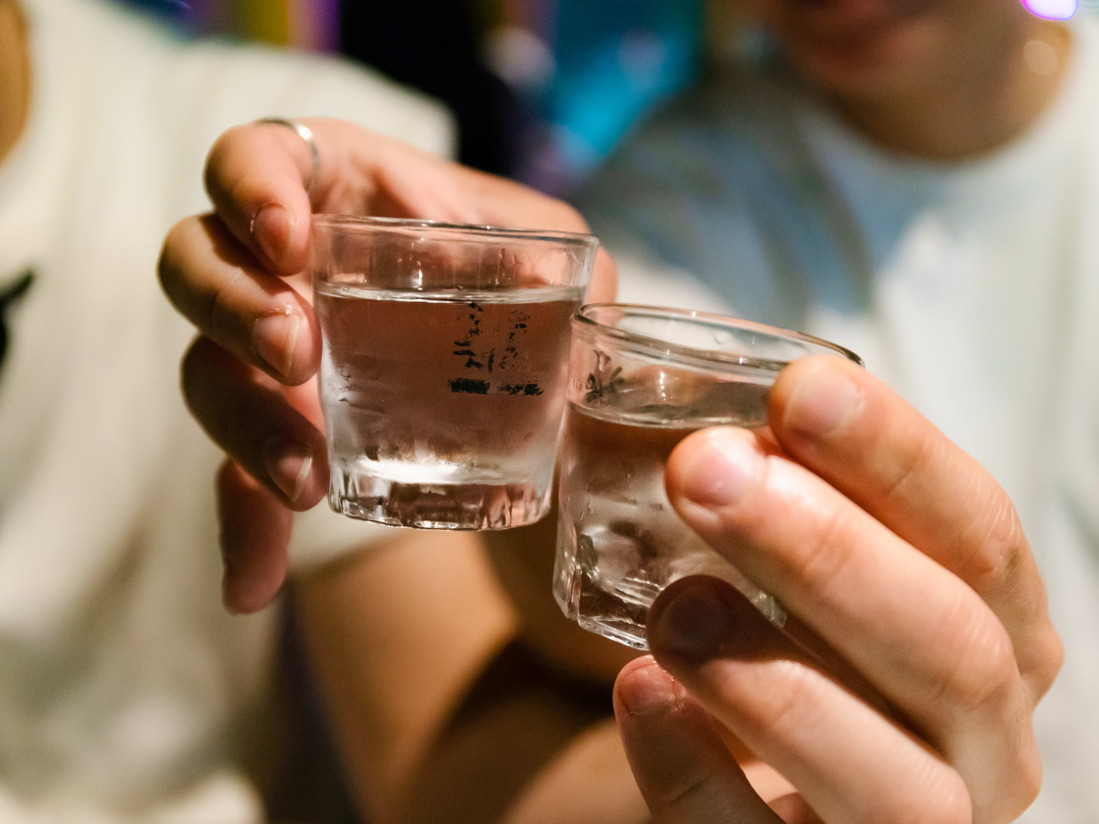 Two people cheers with shot glasses.