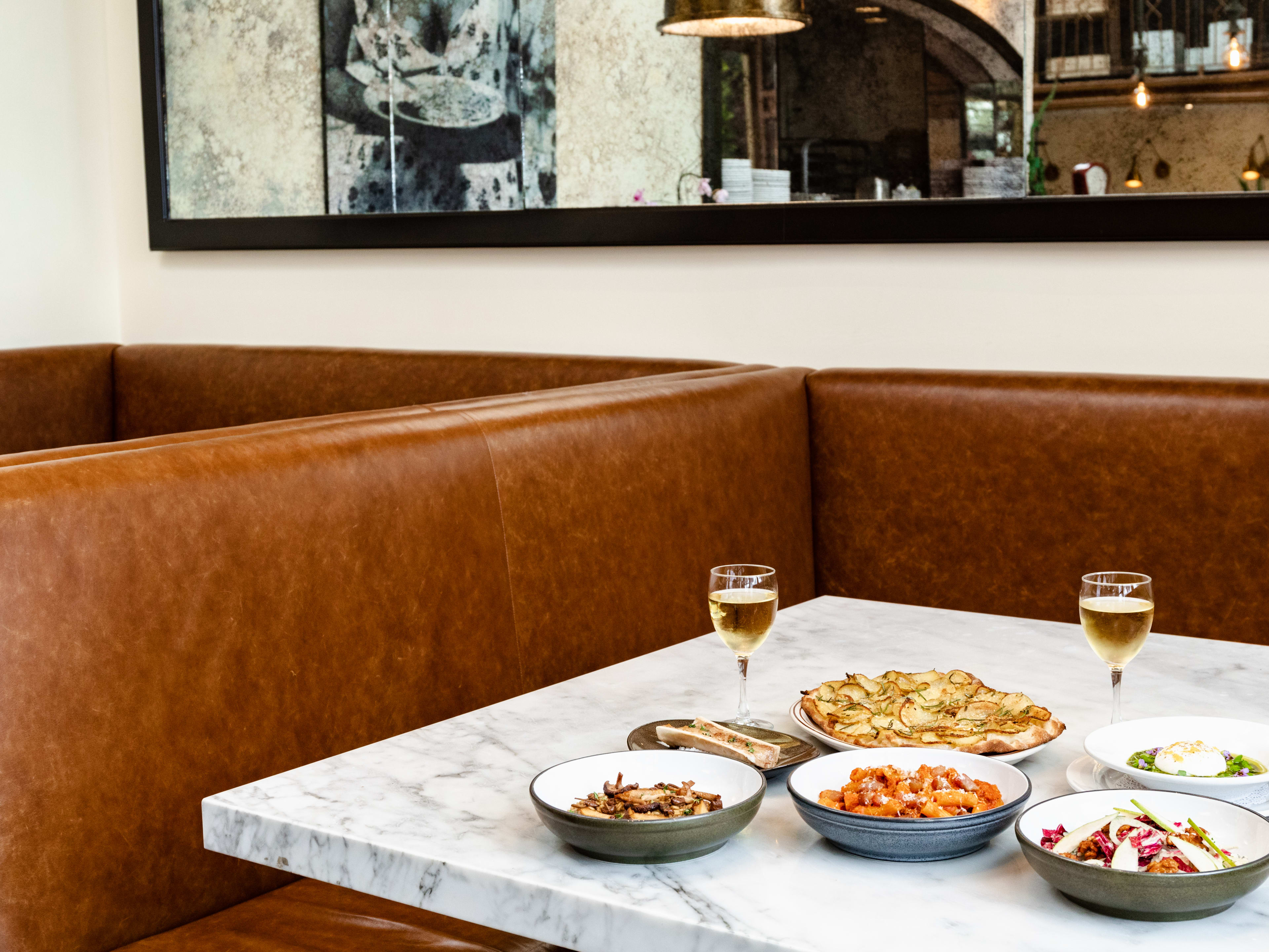 A spread of dishes served on a marble table at a brown leather booth.