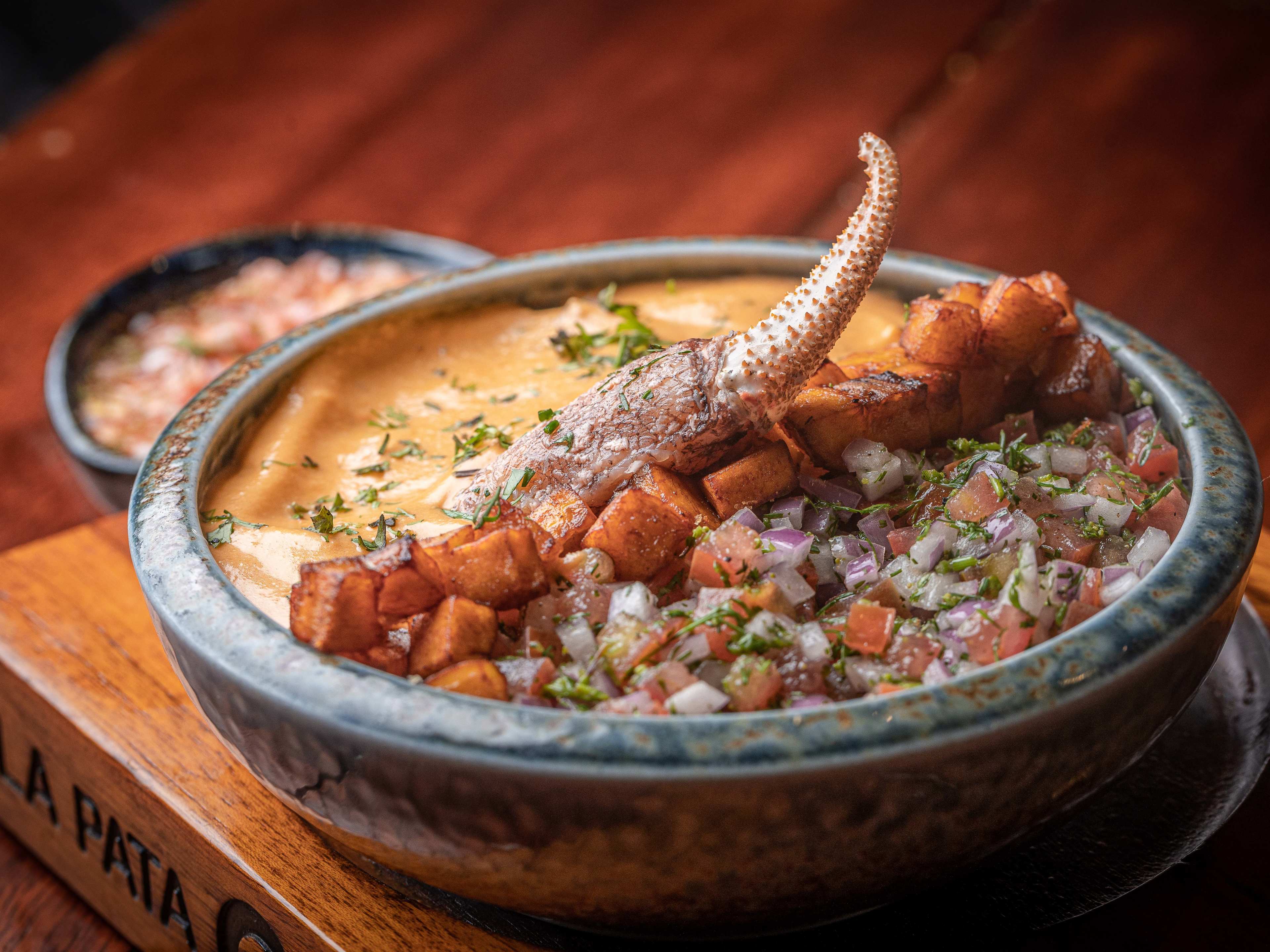 a rice bowl with a crab claw, pico de gallo, yellow sauce, and plantain cubes.