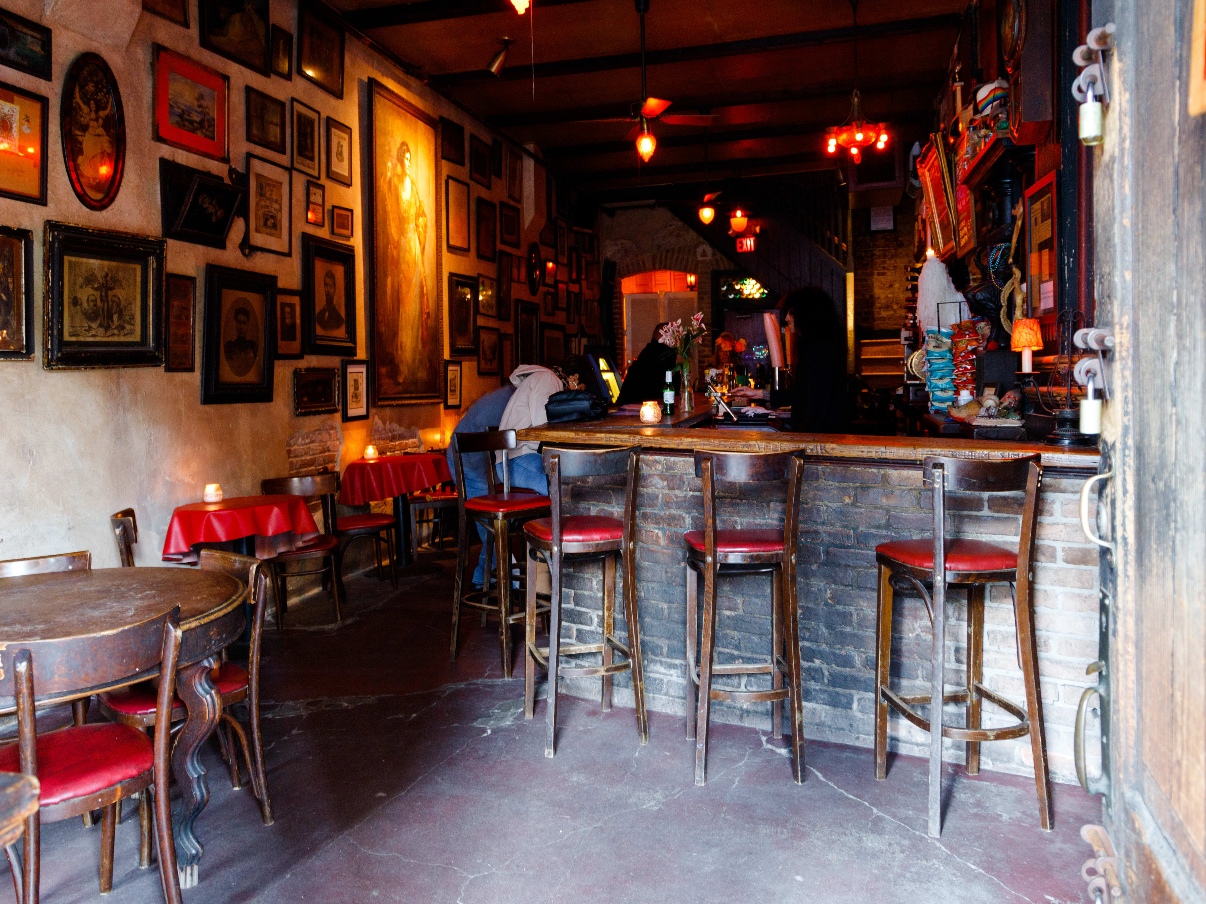 People sit at the wooden bar at La Carafe. Small tables with red tablecloths line the frame covered wall.