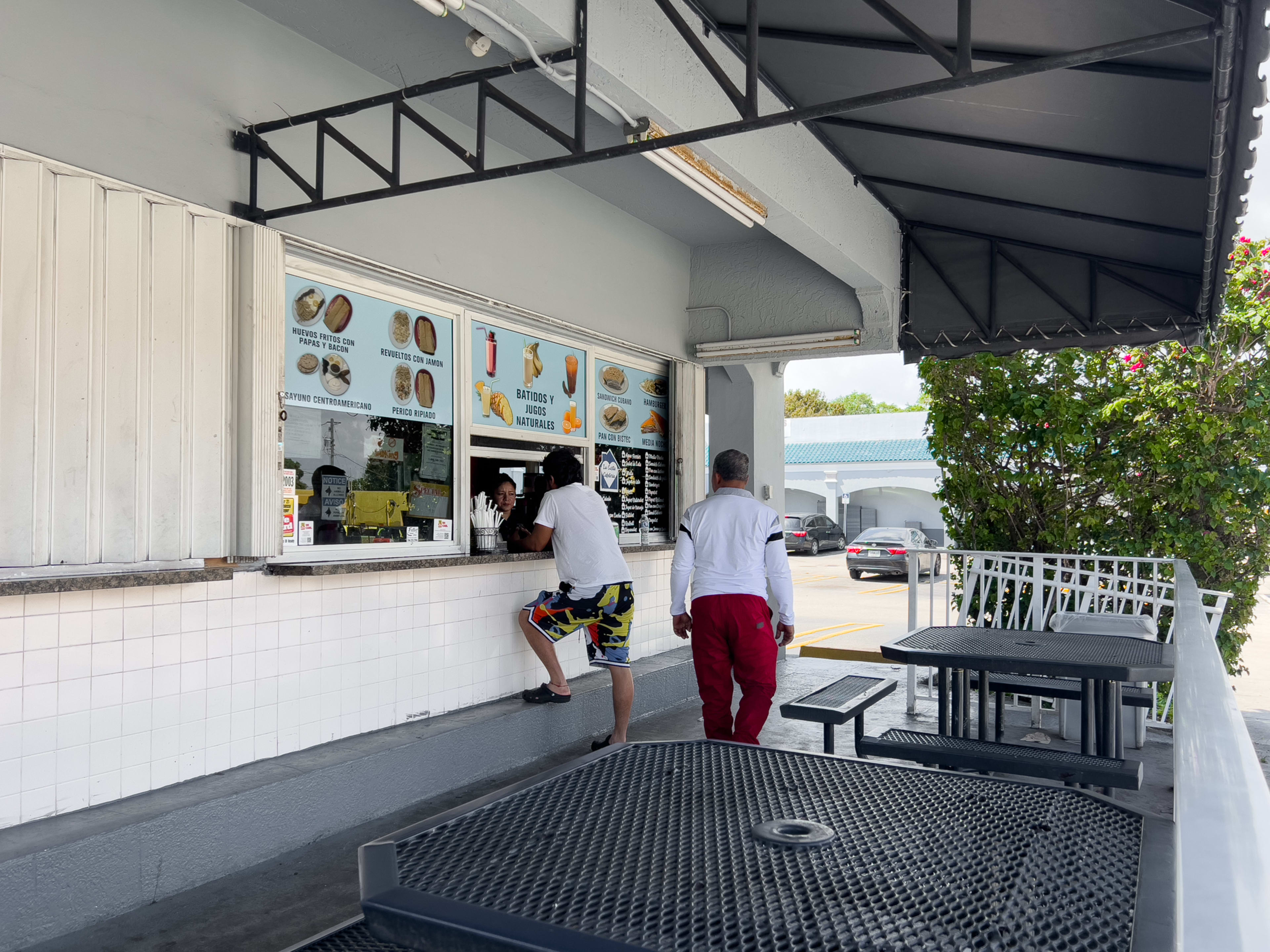 An outdoor window where you can order food from and two black tables.